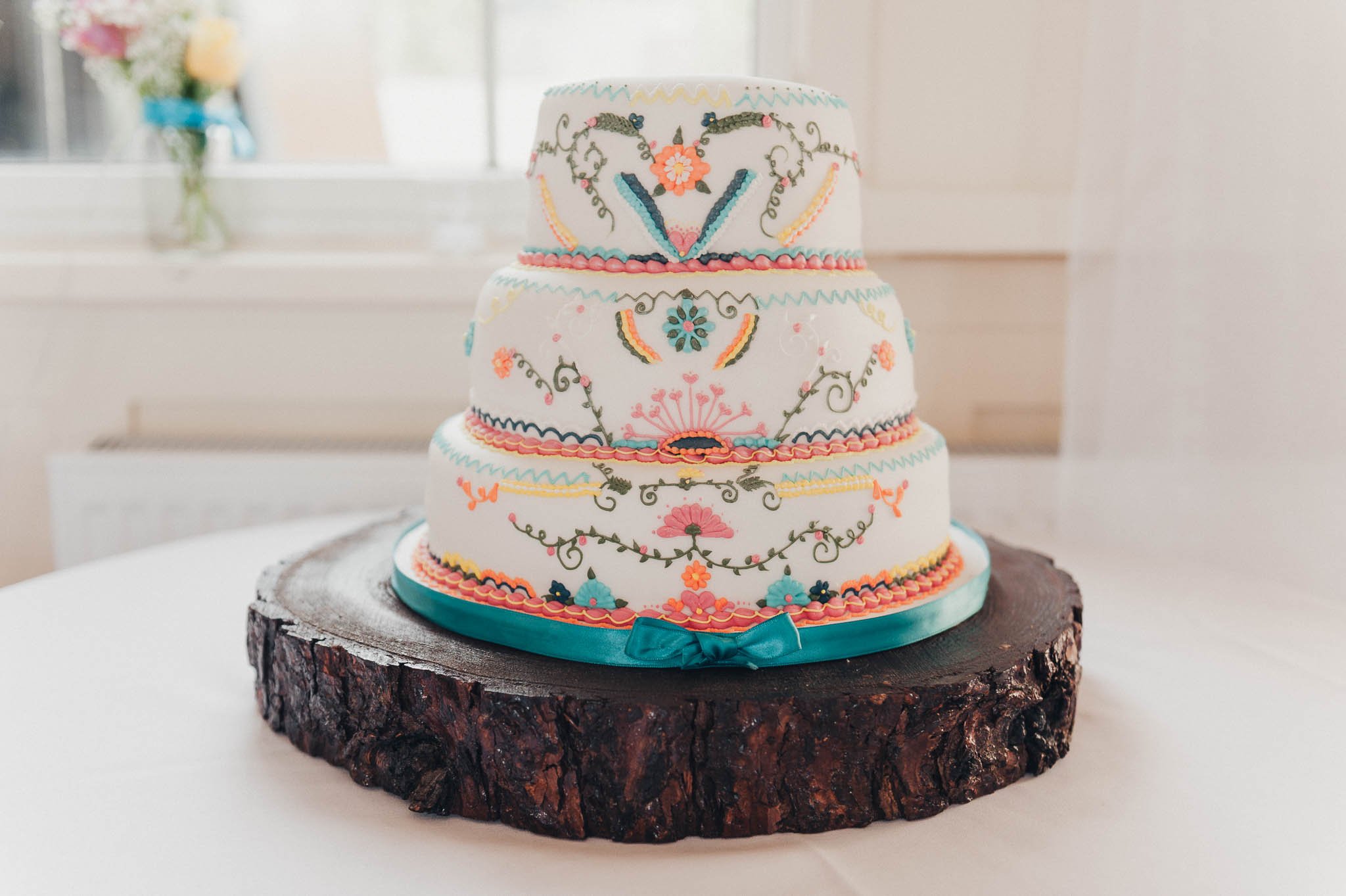 A tiered wedding cake decorated with colourful floral patterns on a wooden stand.