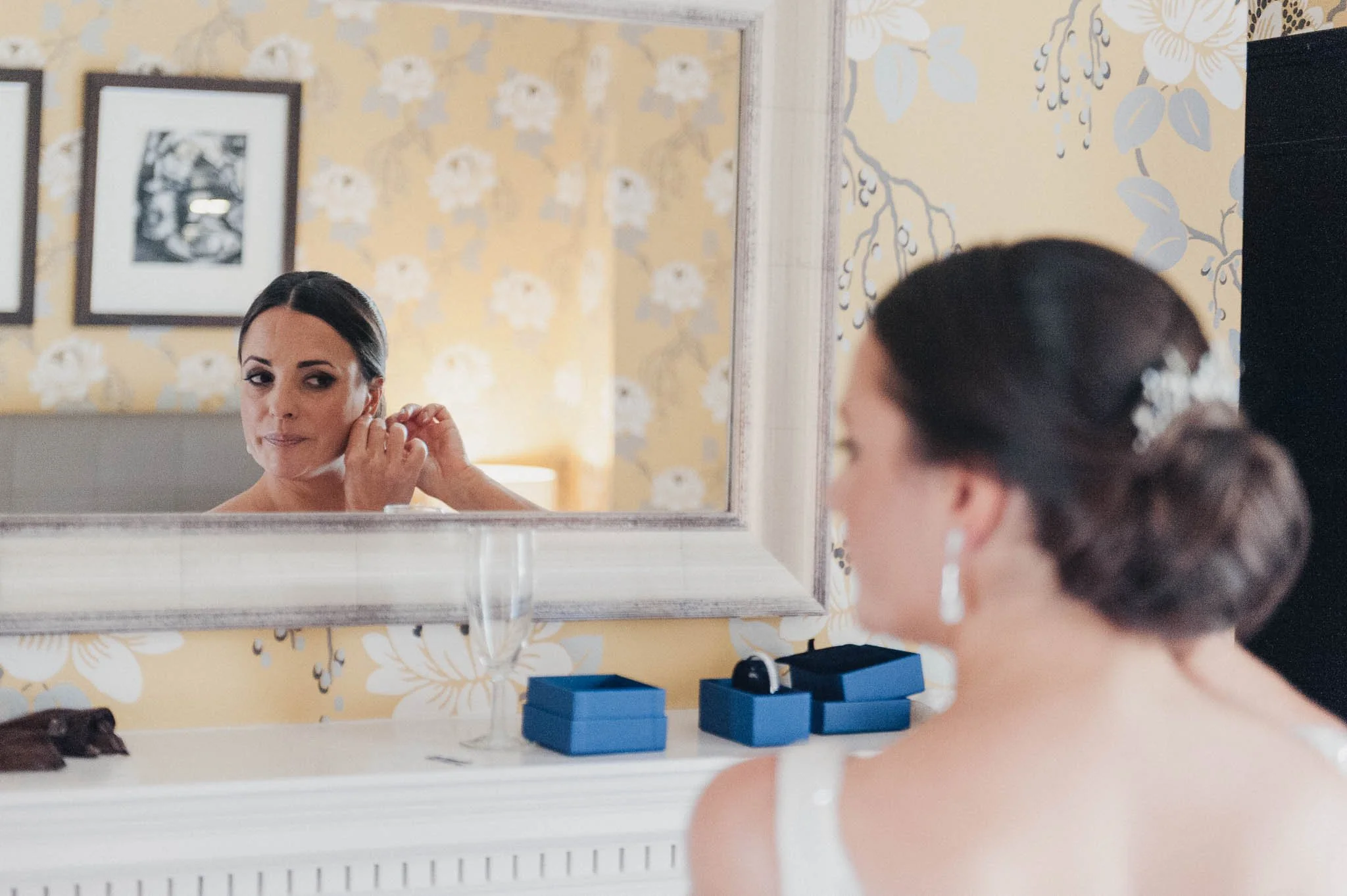 Bride looking into a mirror as she adjusts an earring during the getting-ready moments.