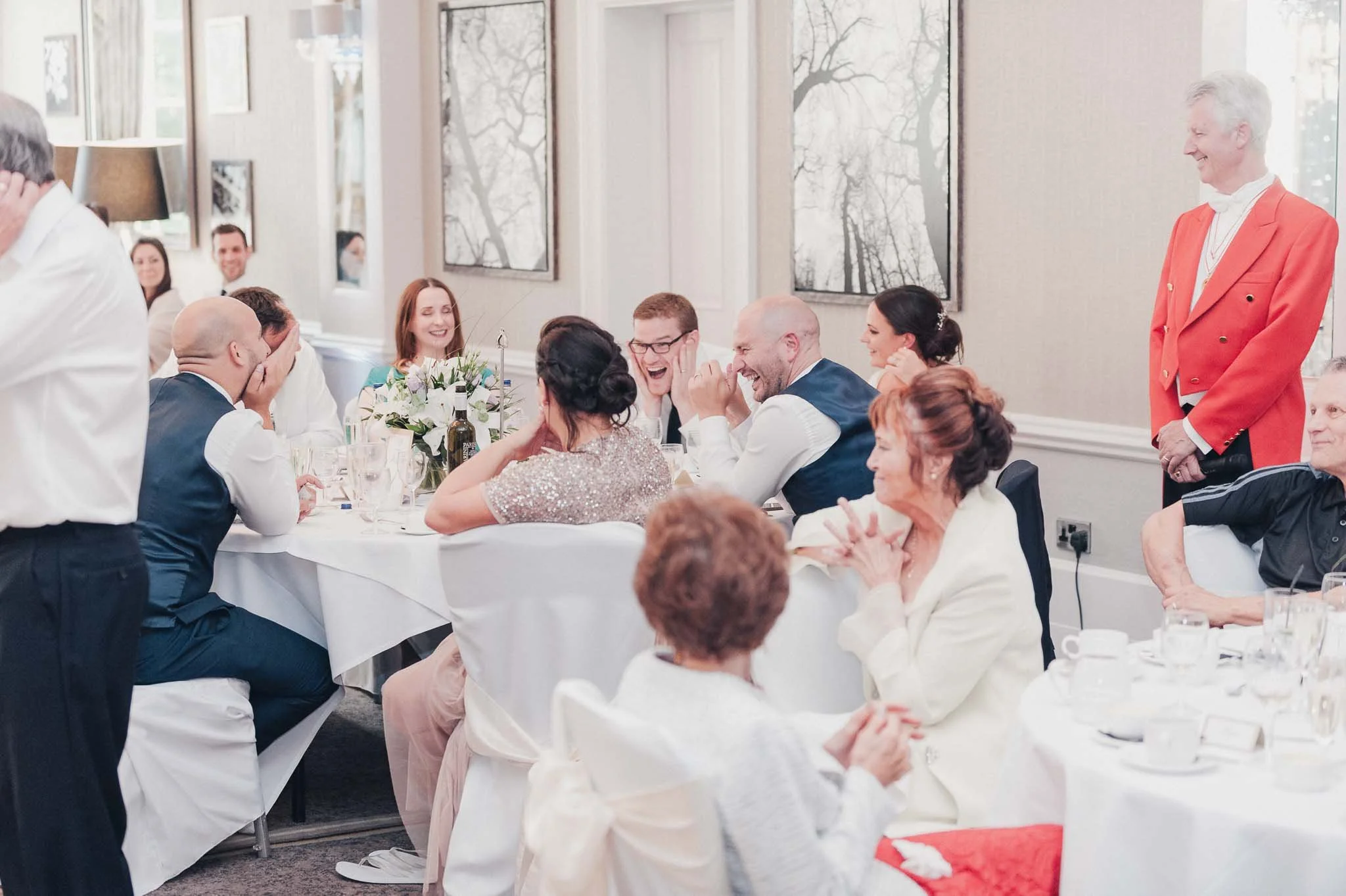 Tables of guests laughing and reacting during the wedding speeches.
