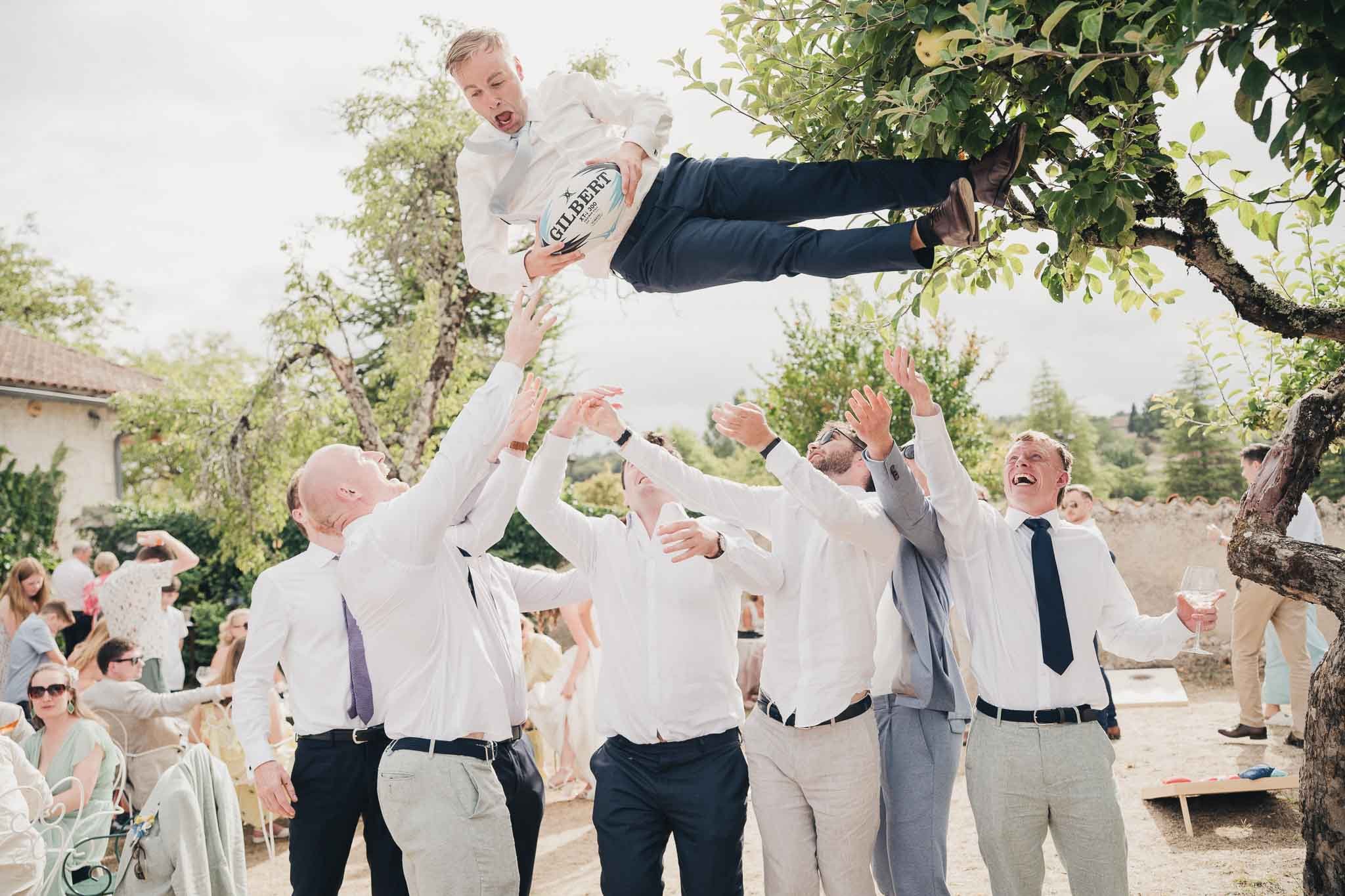 Groomsmen lifting a guest into the air during a playful moment at the Manoir de Longeveau reception.