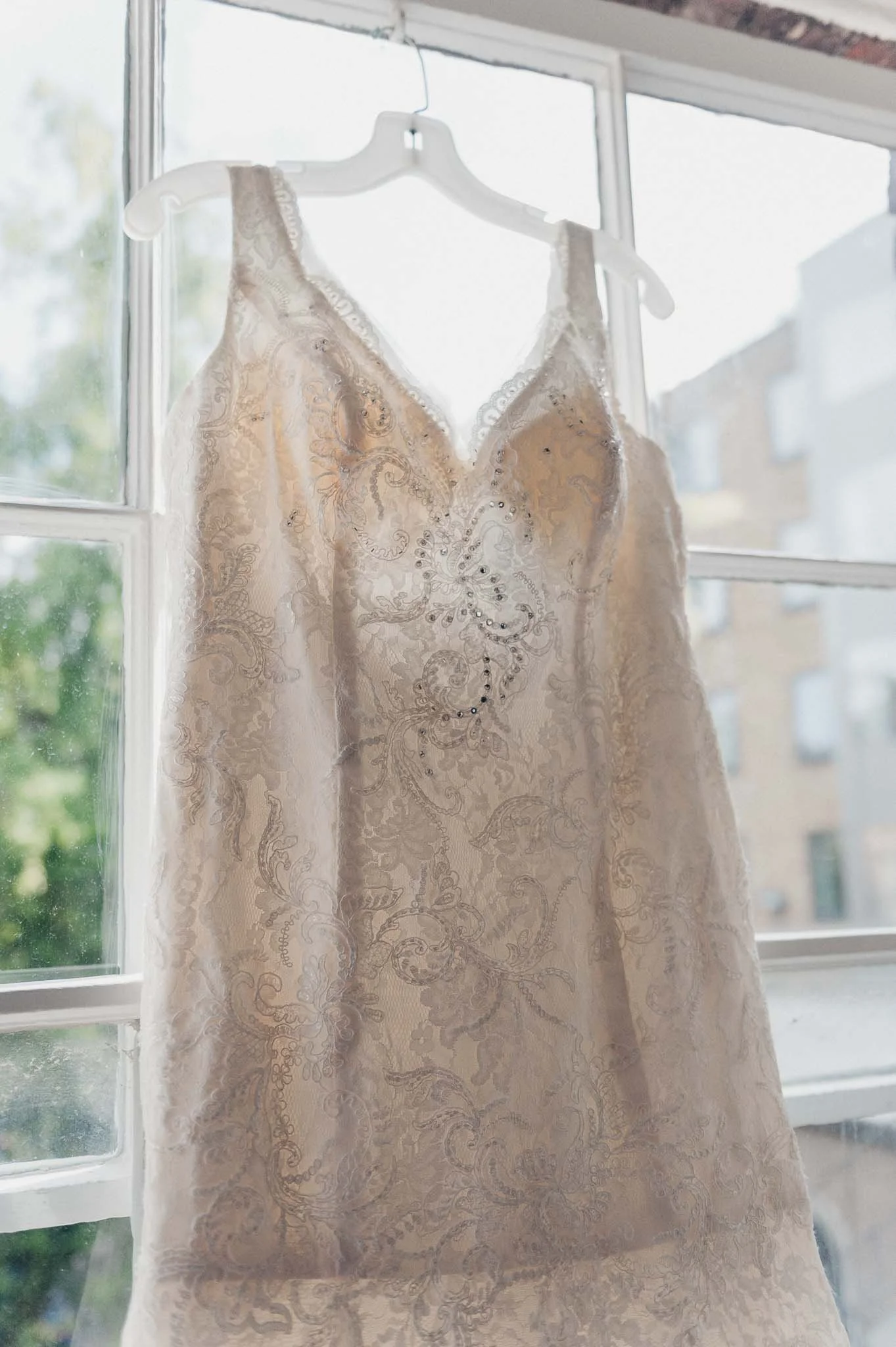 Bride’s dress hanging in front of a window during the morning preparations