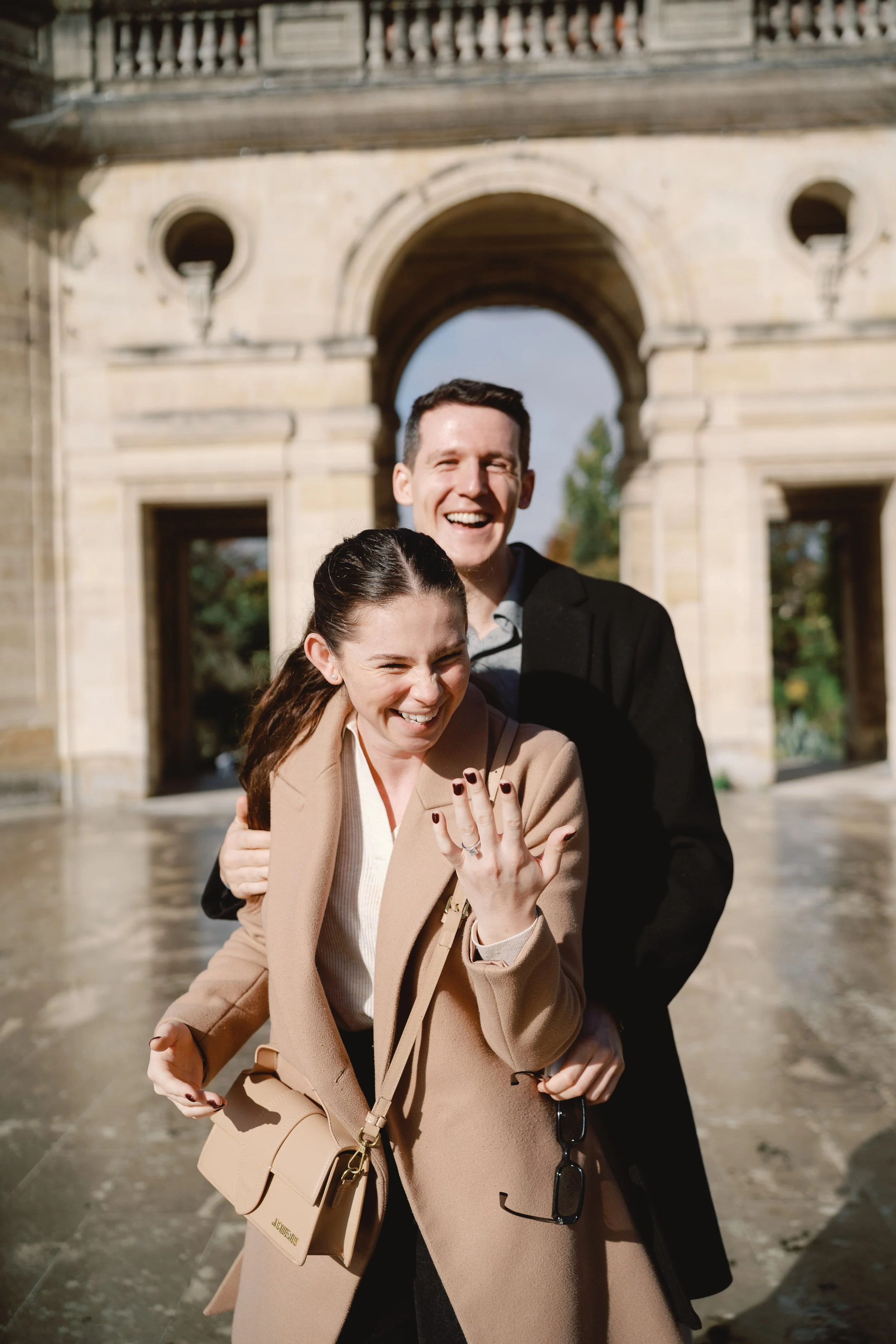 Couple laughing together immediately after a surprise proposal beneath historic architecture in Bordeaux.