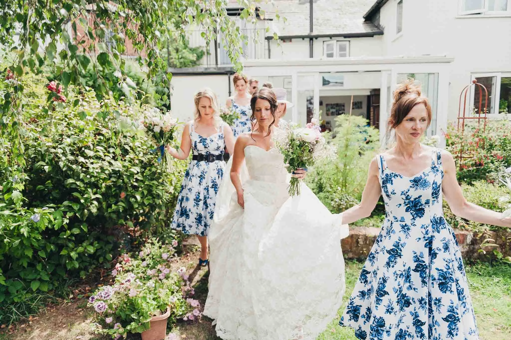 Bridesmaids helping the bride walk through a garden path on the way to the ceremony.