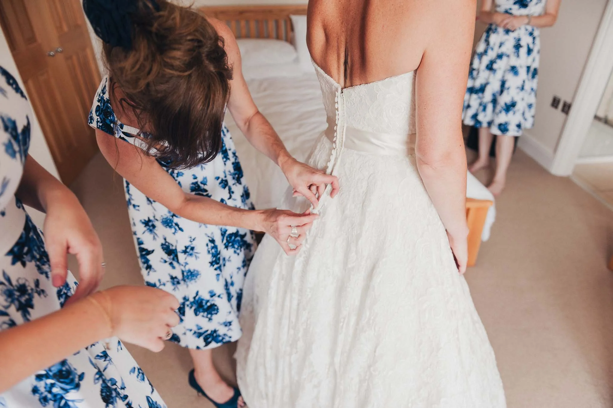 The bride having her wedding dress fastened by a bridesmaid during morning prep.