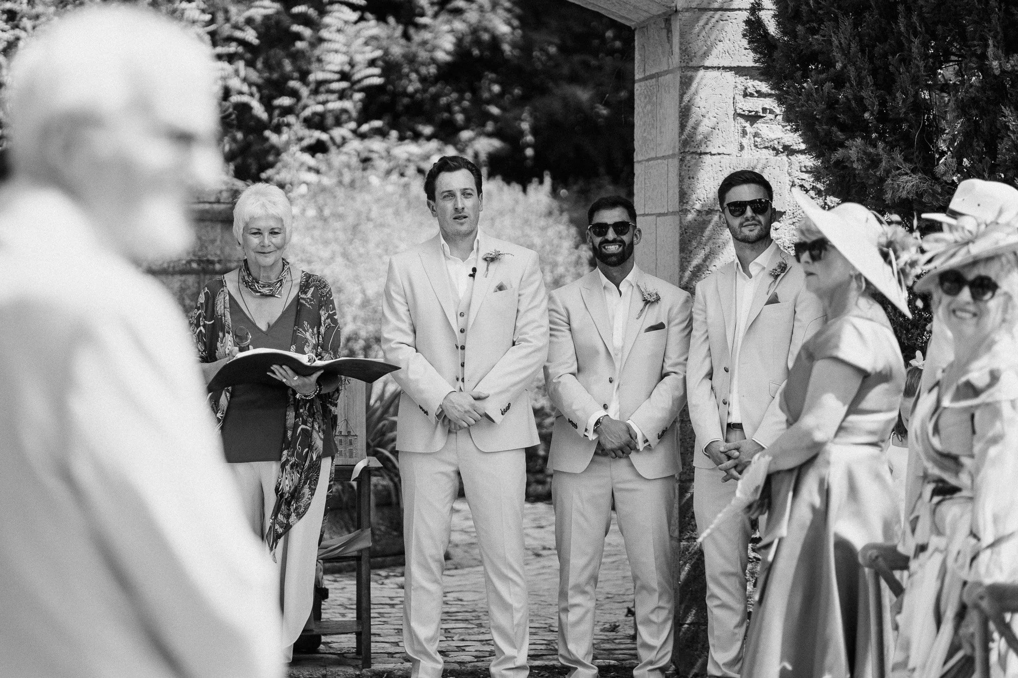 Celebrant and groomsmen waiting at the outdoor wedding ceremony, captured in black and white.