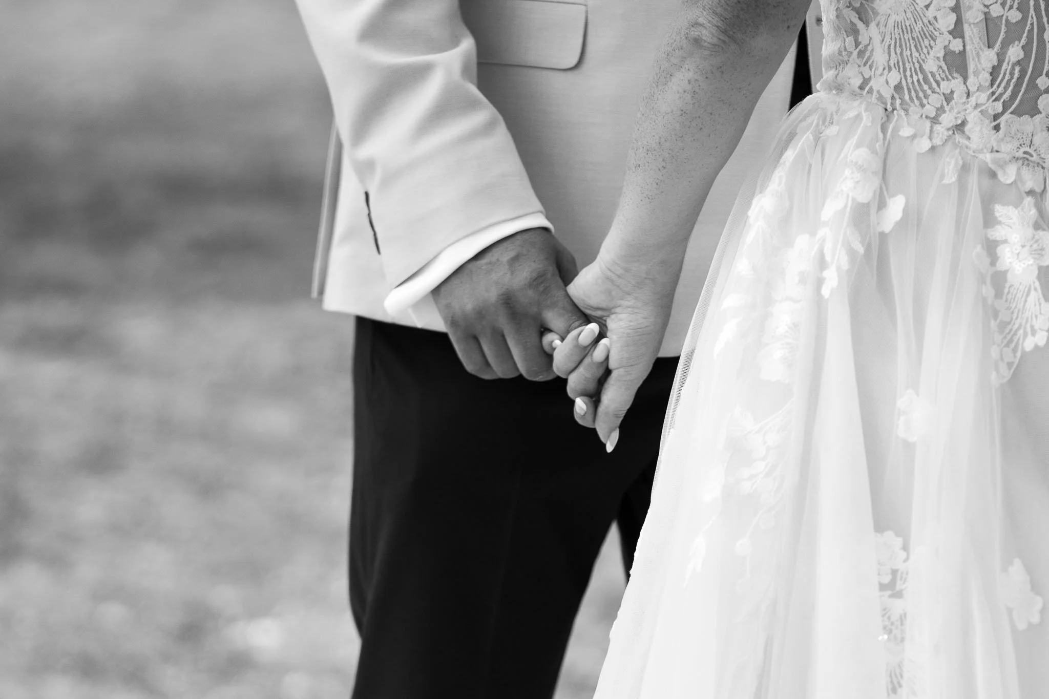 Black and white photograph of bride and groom's clasped hands while walking at Paradis des Vignes, Charente