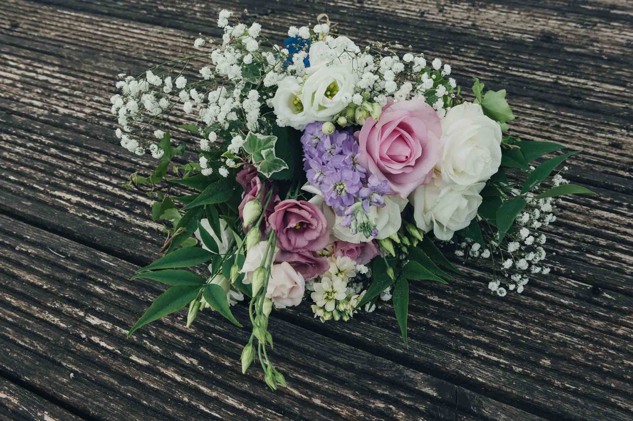 Bridal bouquet with roses, lisianthus and greenery placed on wooden decking.