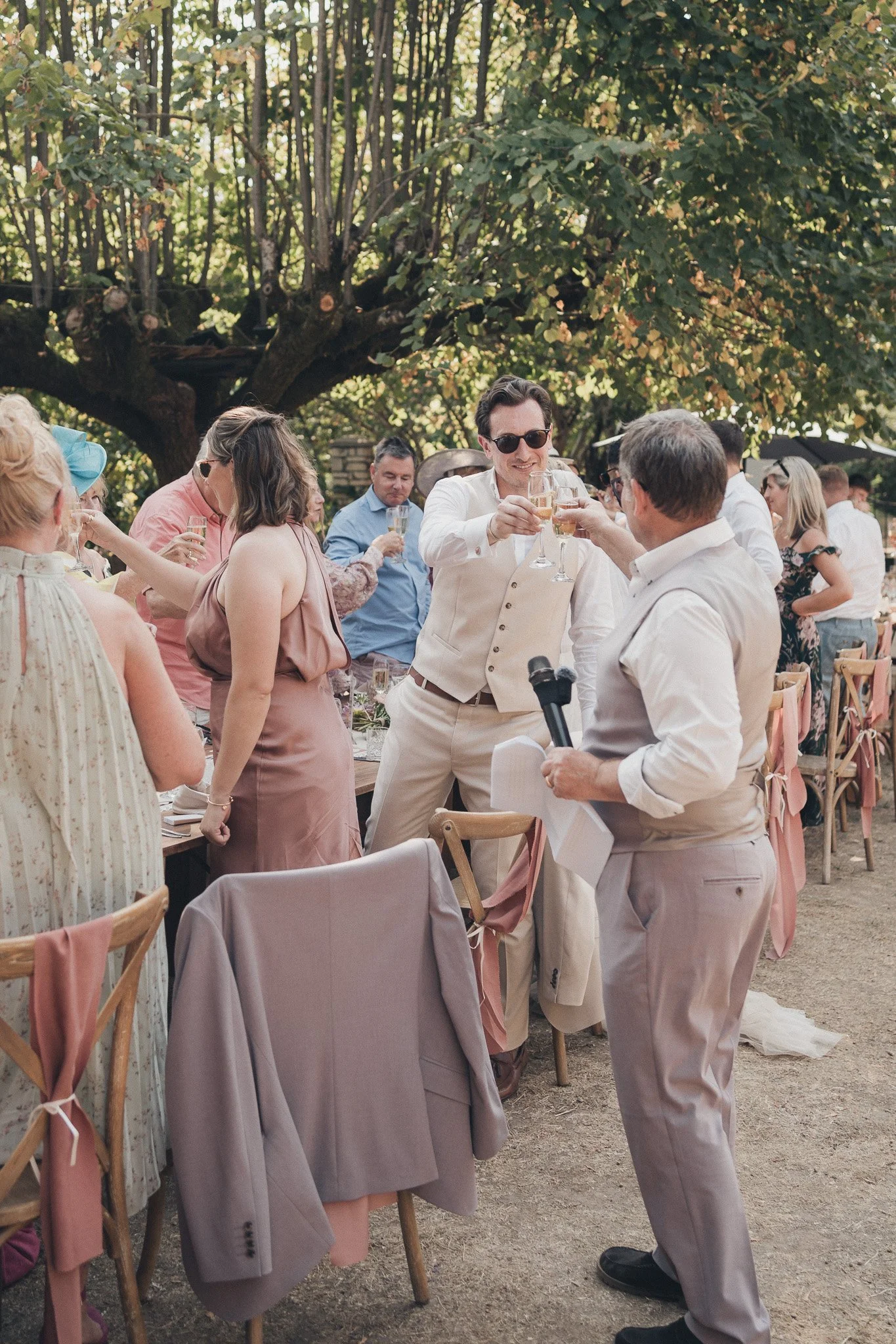 “A lively moment during the outdoor wedding meal with guests raising glasses and celebrating.