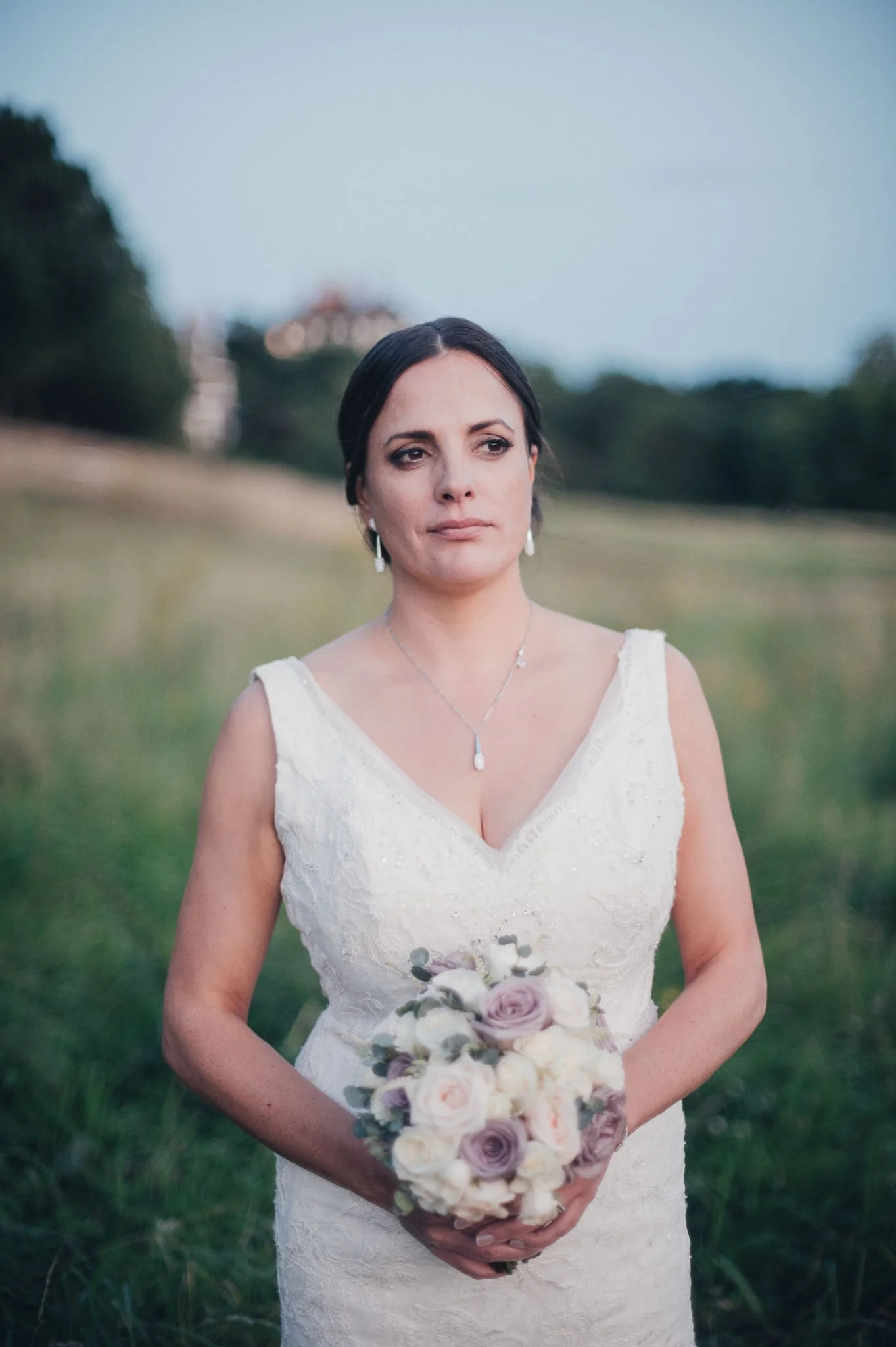 Portrait of the bride standing in a field holding her bouquet.