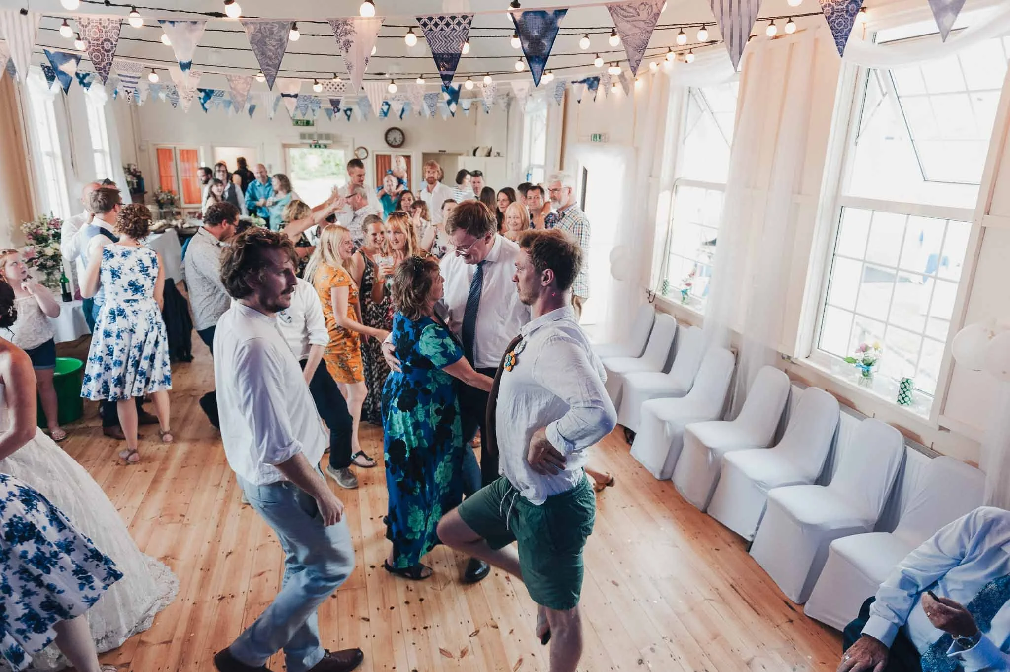 Guests dancing enthusiastically on the reception dance floor inside the village hall.