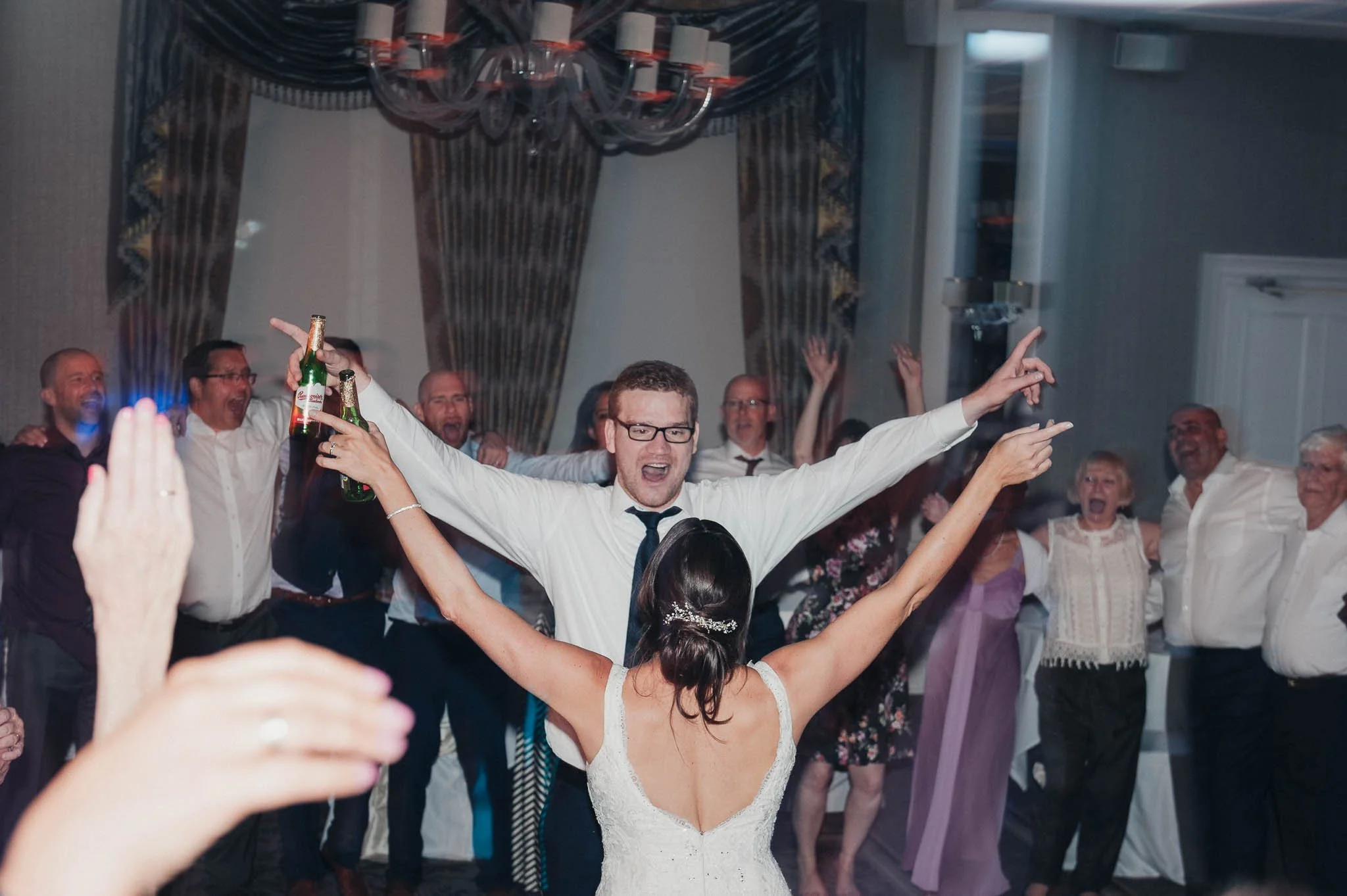 The groom with arms outstretched as the bride faces him during a joyful dance floor moment.