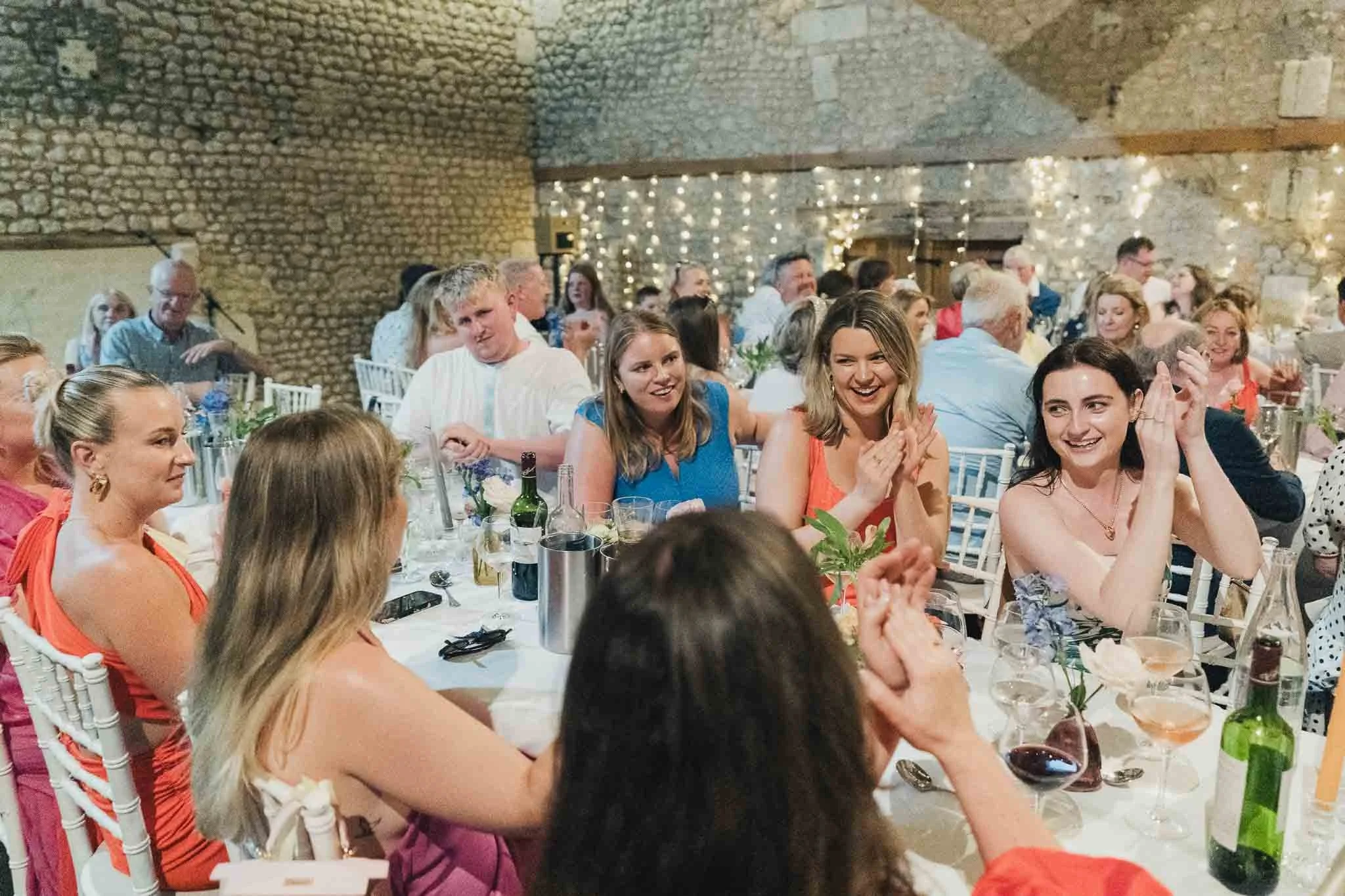 Guests clapping and smiling at their tables during the wedding dinner.