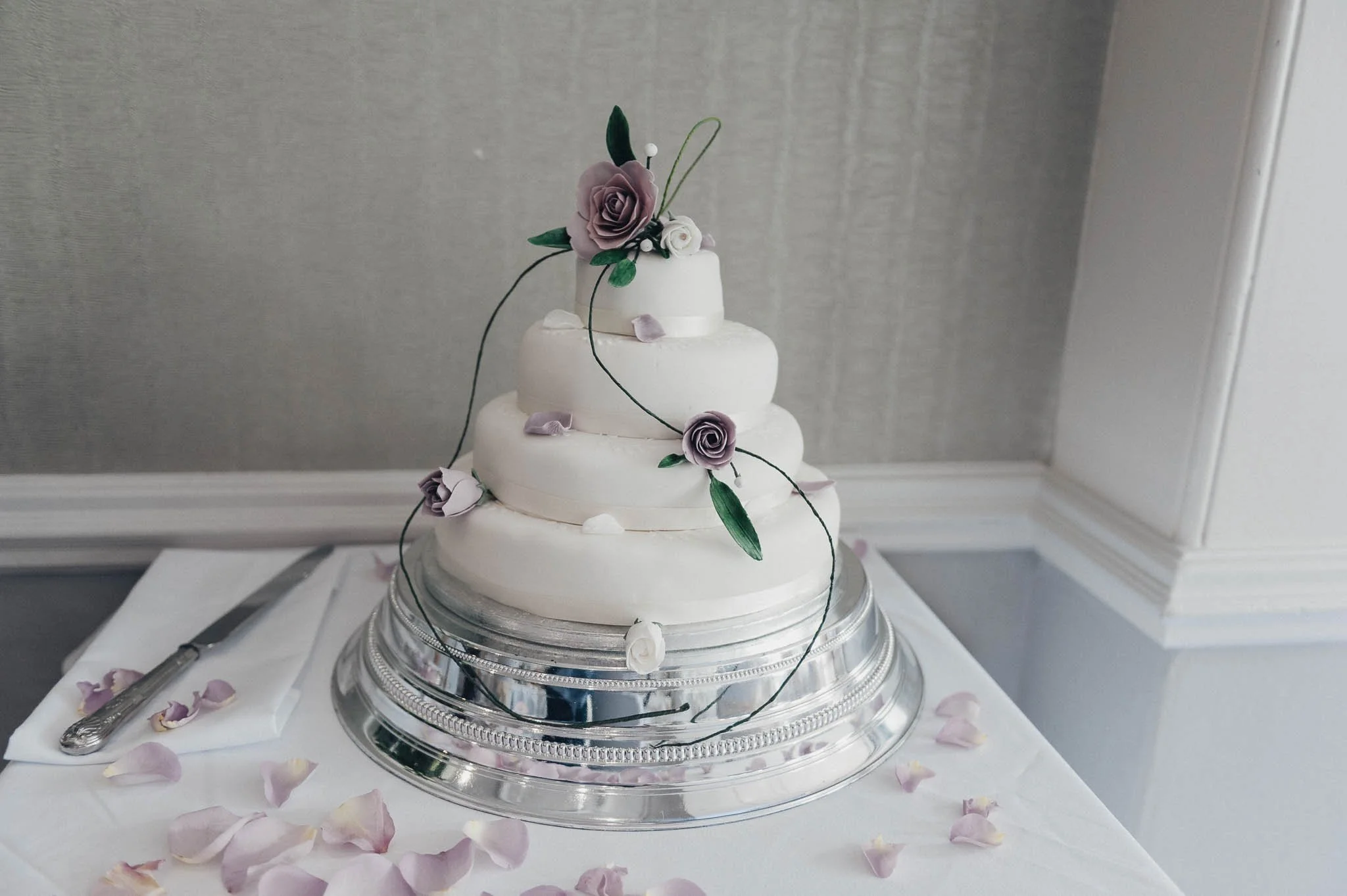 Three-tier white wedding cake decorated with purple flowers, displayed before the reception.