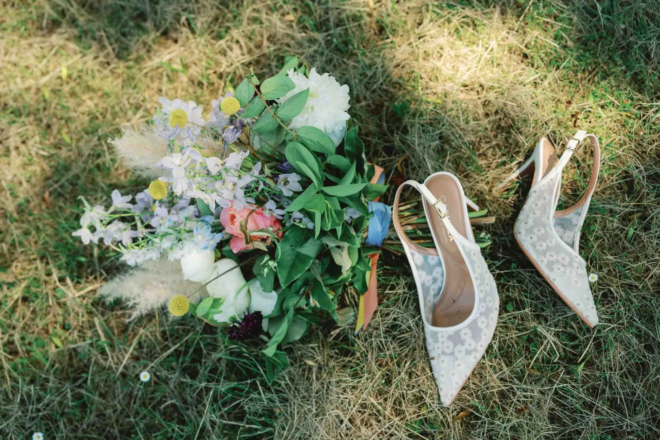 Bridal bouquet and wedding shoes laid out in long grass