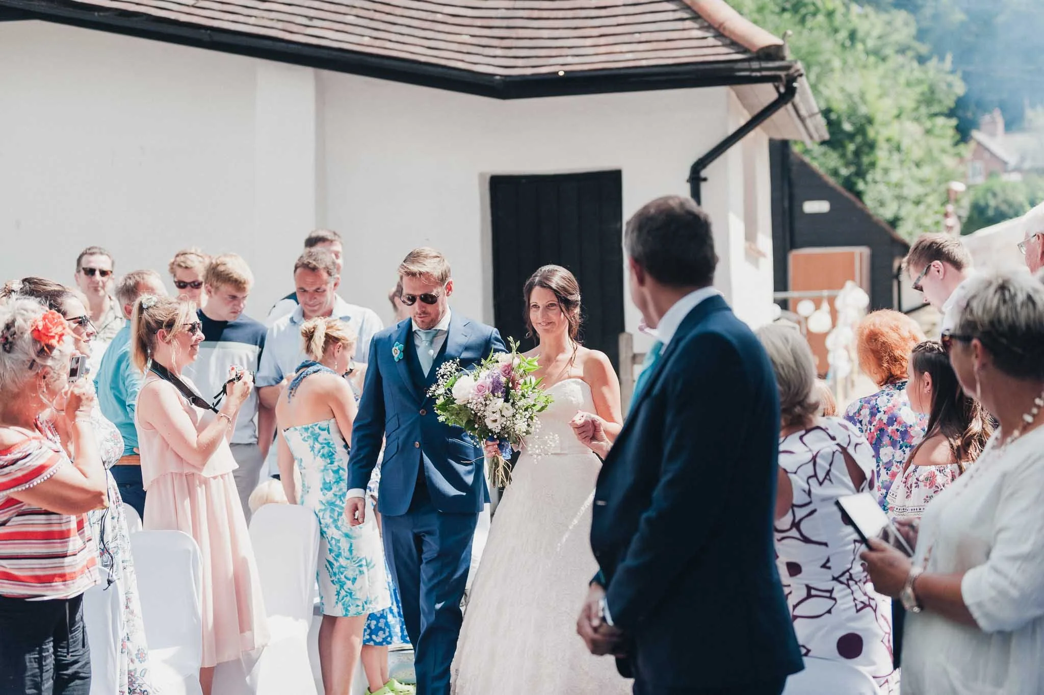 Guests standing as the bride walks down the aisle with her escort at the outdoor ceremony.