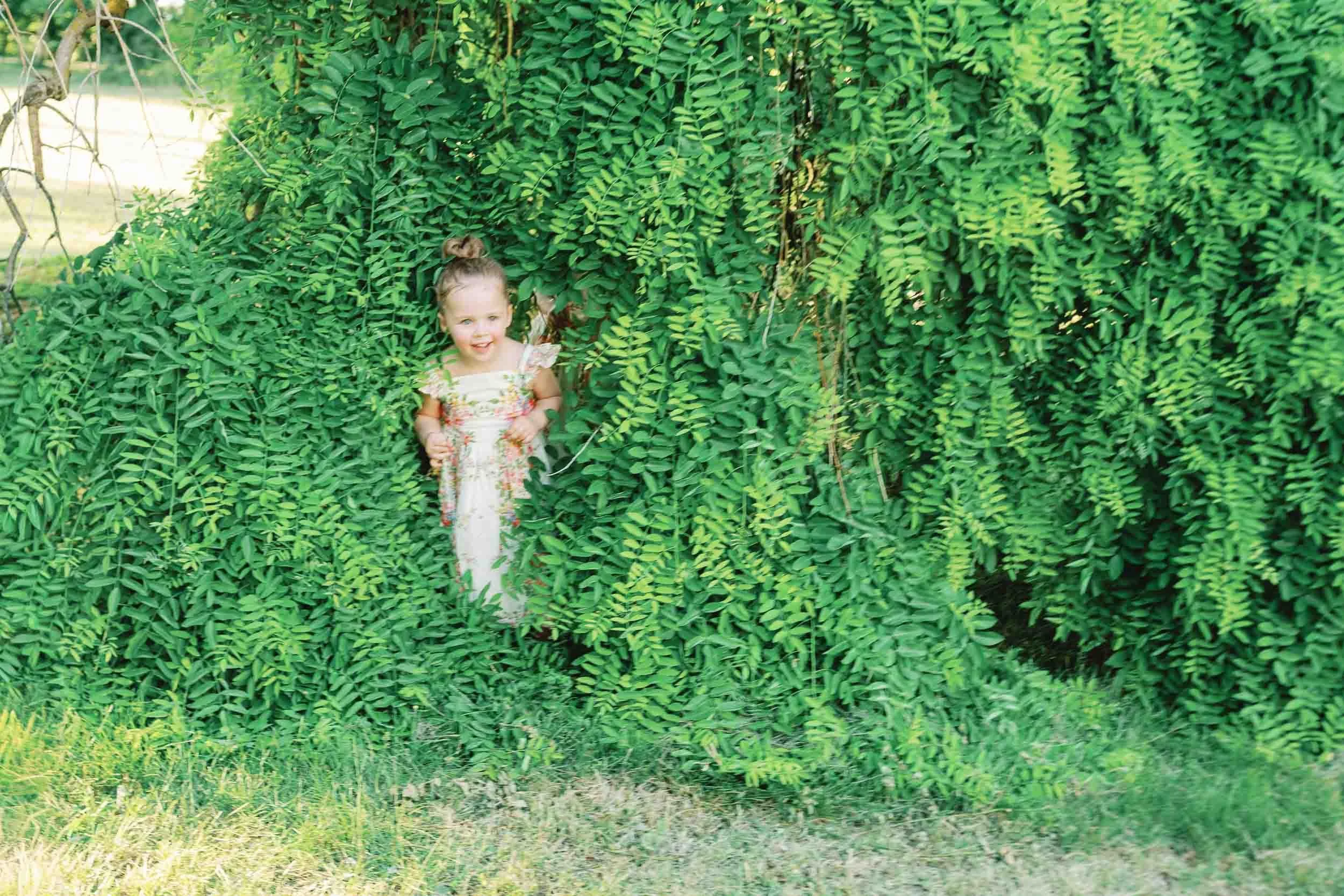 A young flower girl hiding playfully in the bushes