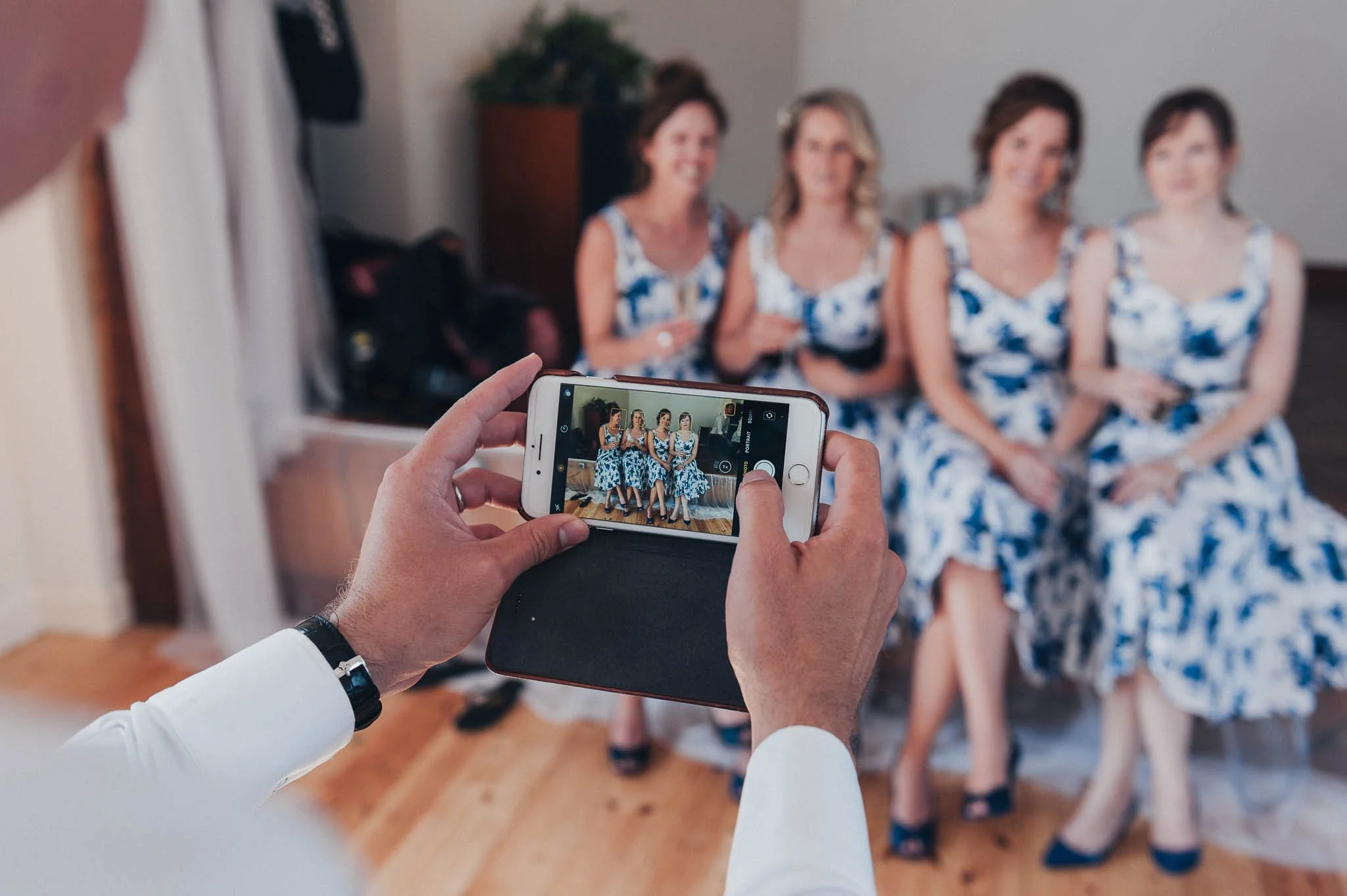 Guest holding a phone to photograph the bridesmaids sitting together inside the reception hall.