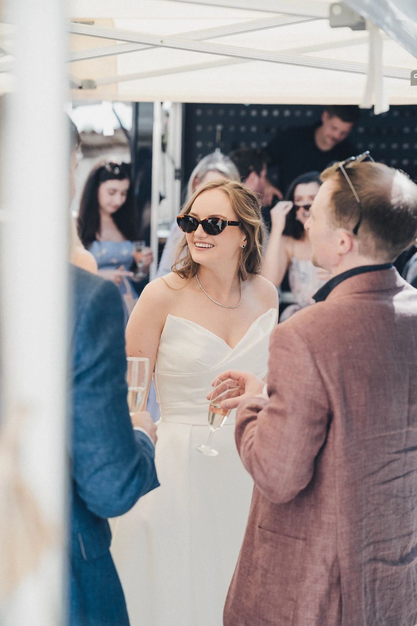 Bride chatting with guests while holding a drink during the reception at Manoir de Longeveau.
