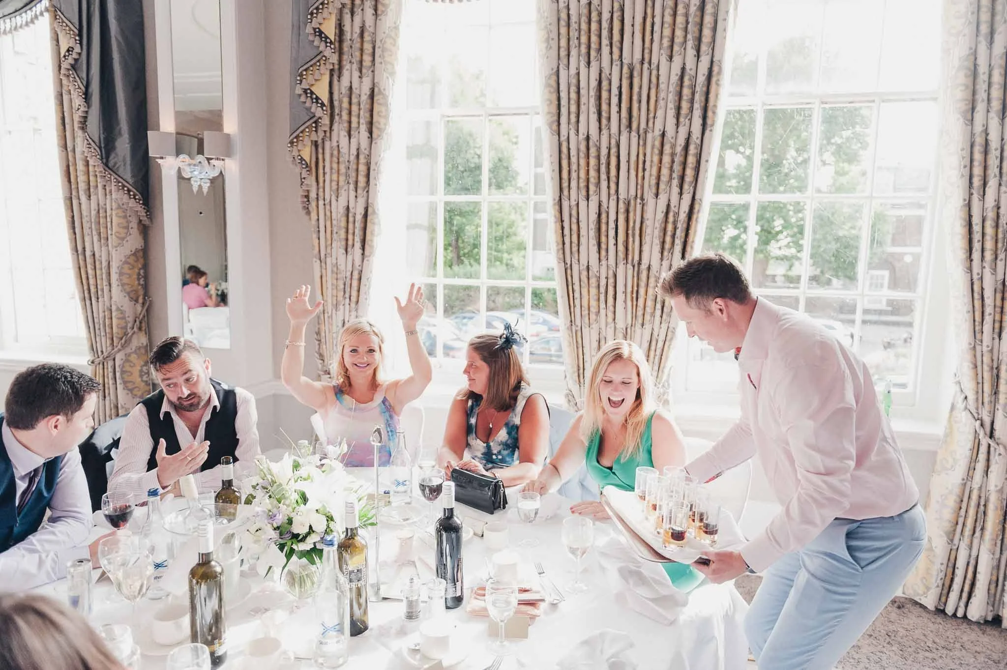 Guests laughing and raising hands during the wedding meal, enjoying the lively atmosphere.
