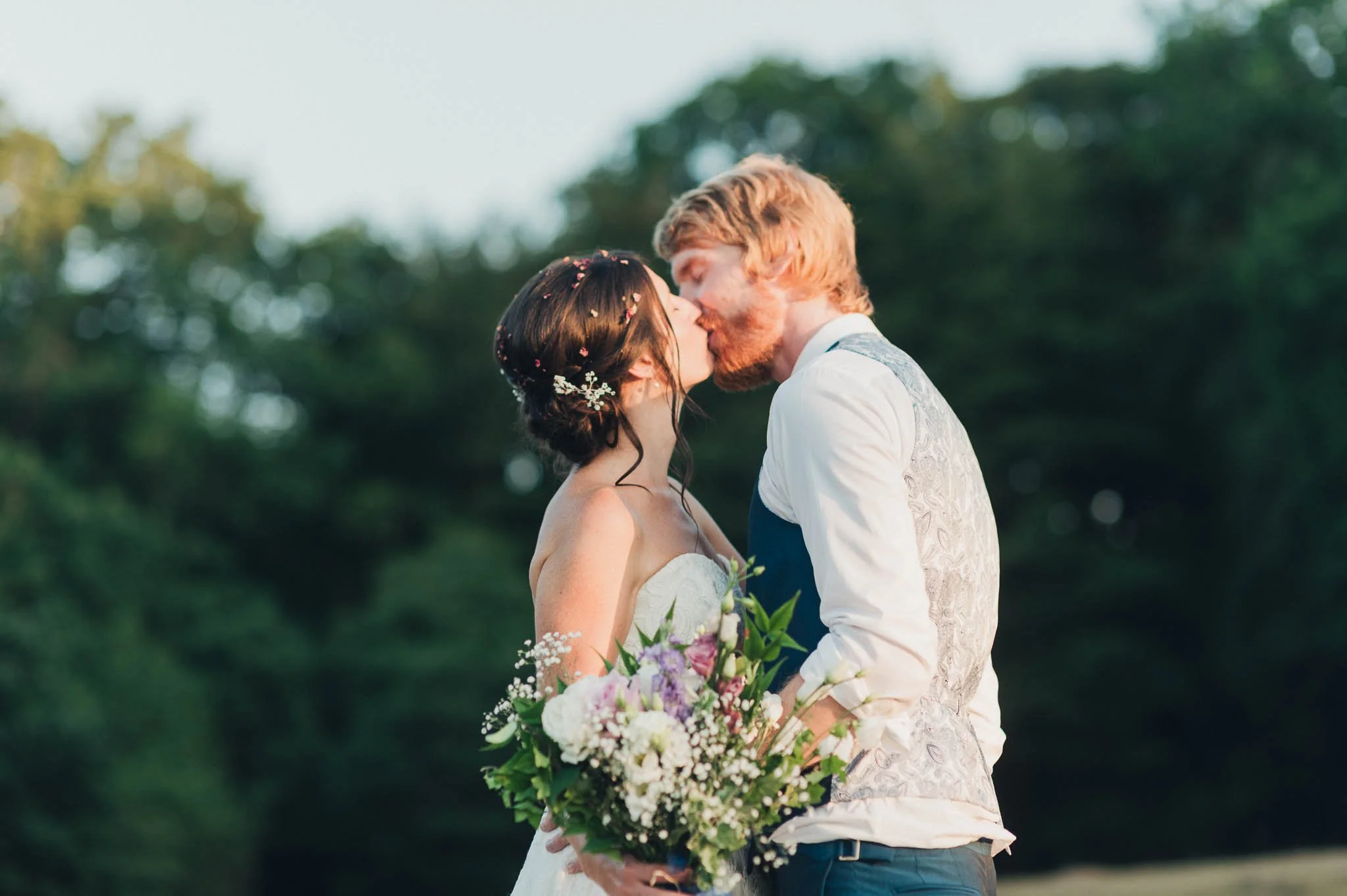 The bride and groom sharing a kiss during their outdoor portraits at sunset.