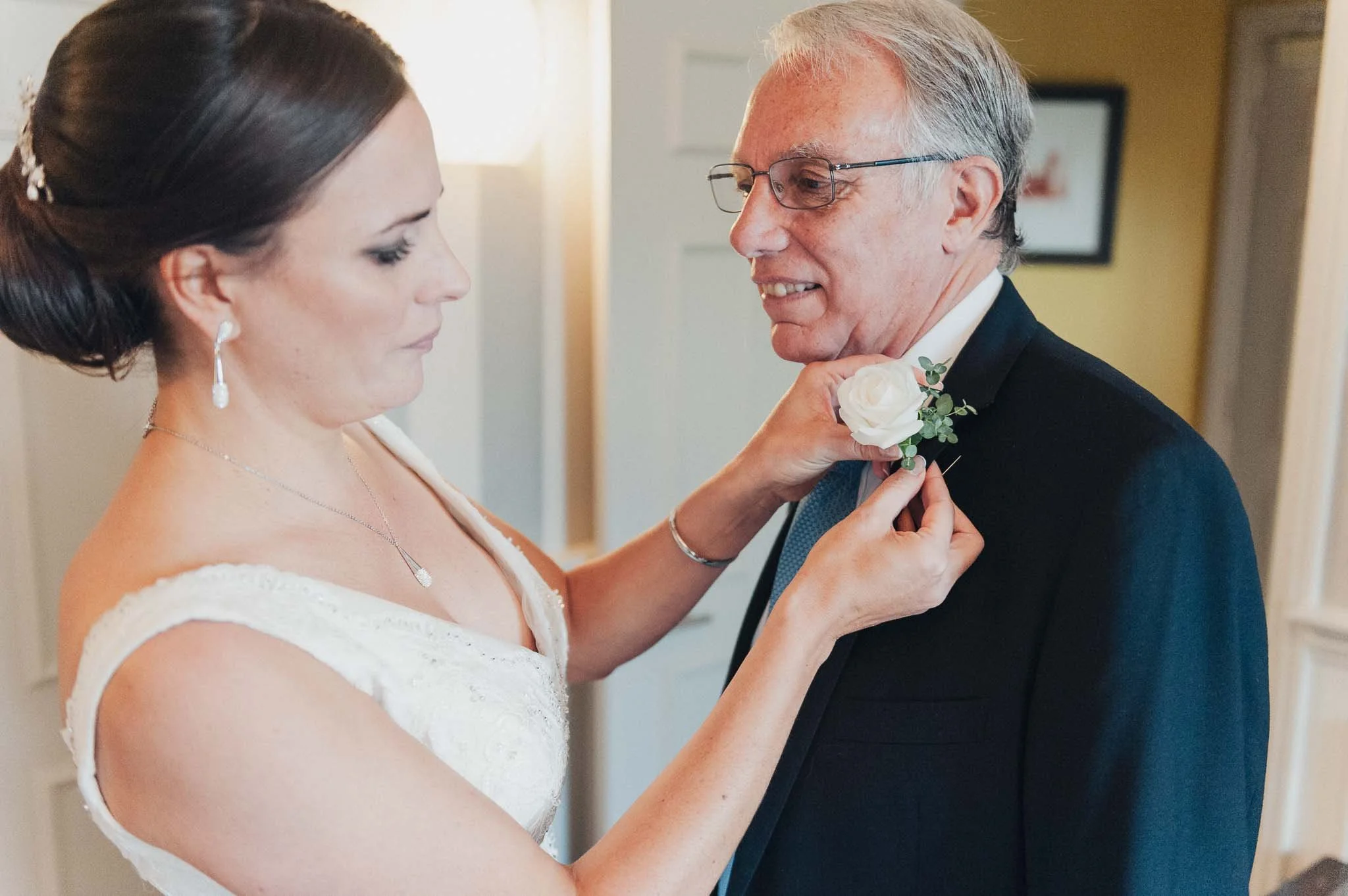 Bride pinning a boutonnière onto a family member’s suit during the morning preparations.