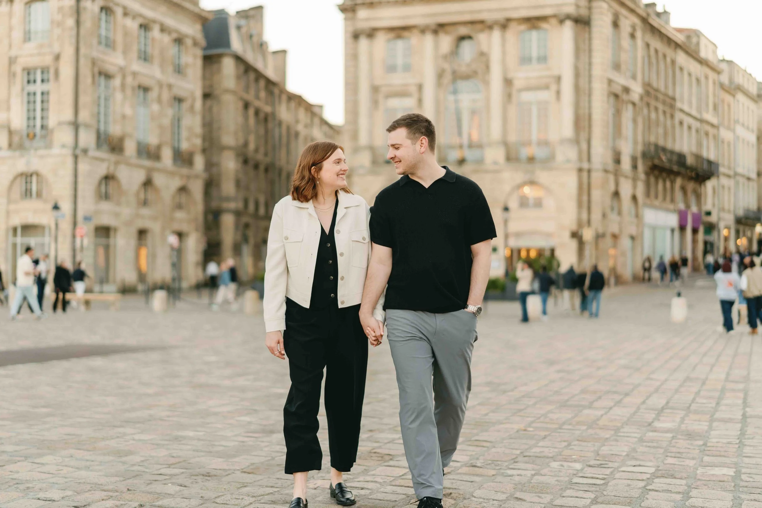 Couple walking hand in hand across a cobbled square in central Bordeaux after their proposal