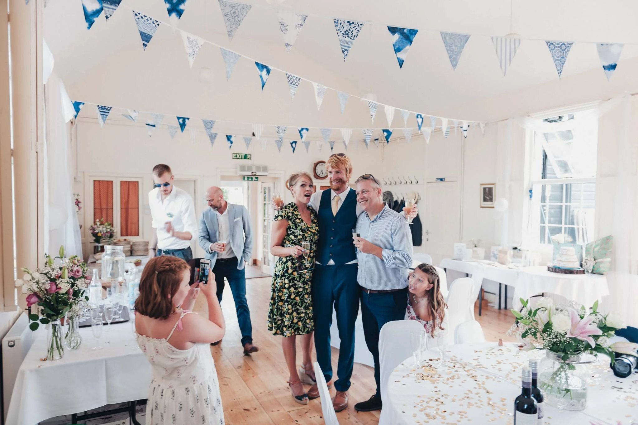 The groom posing with guests inside the decorated village hall.
