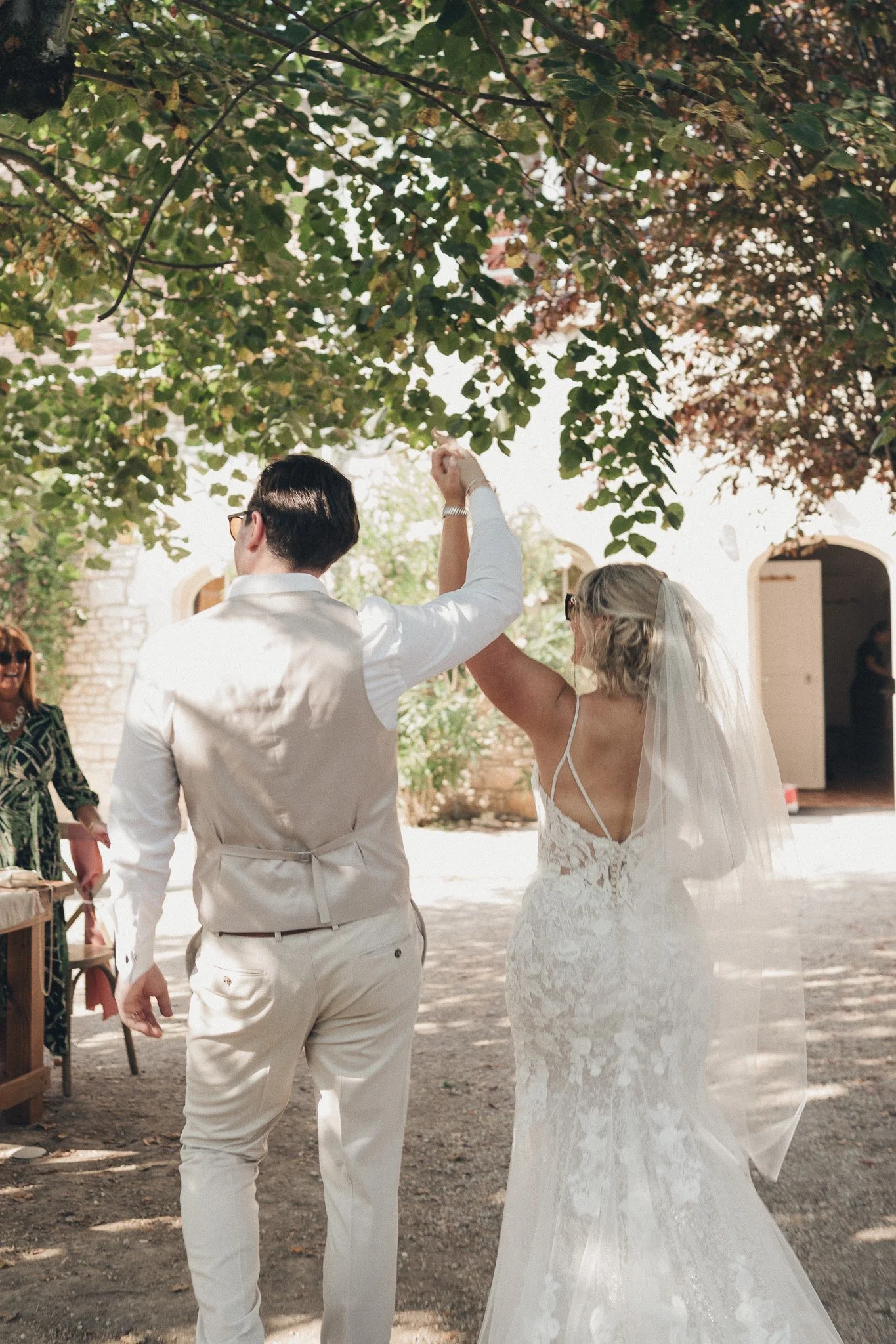 The couple walking hand in hand through the courtyard beneath tree branches after their ceremony.