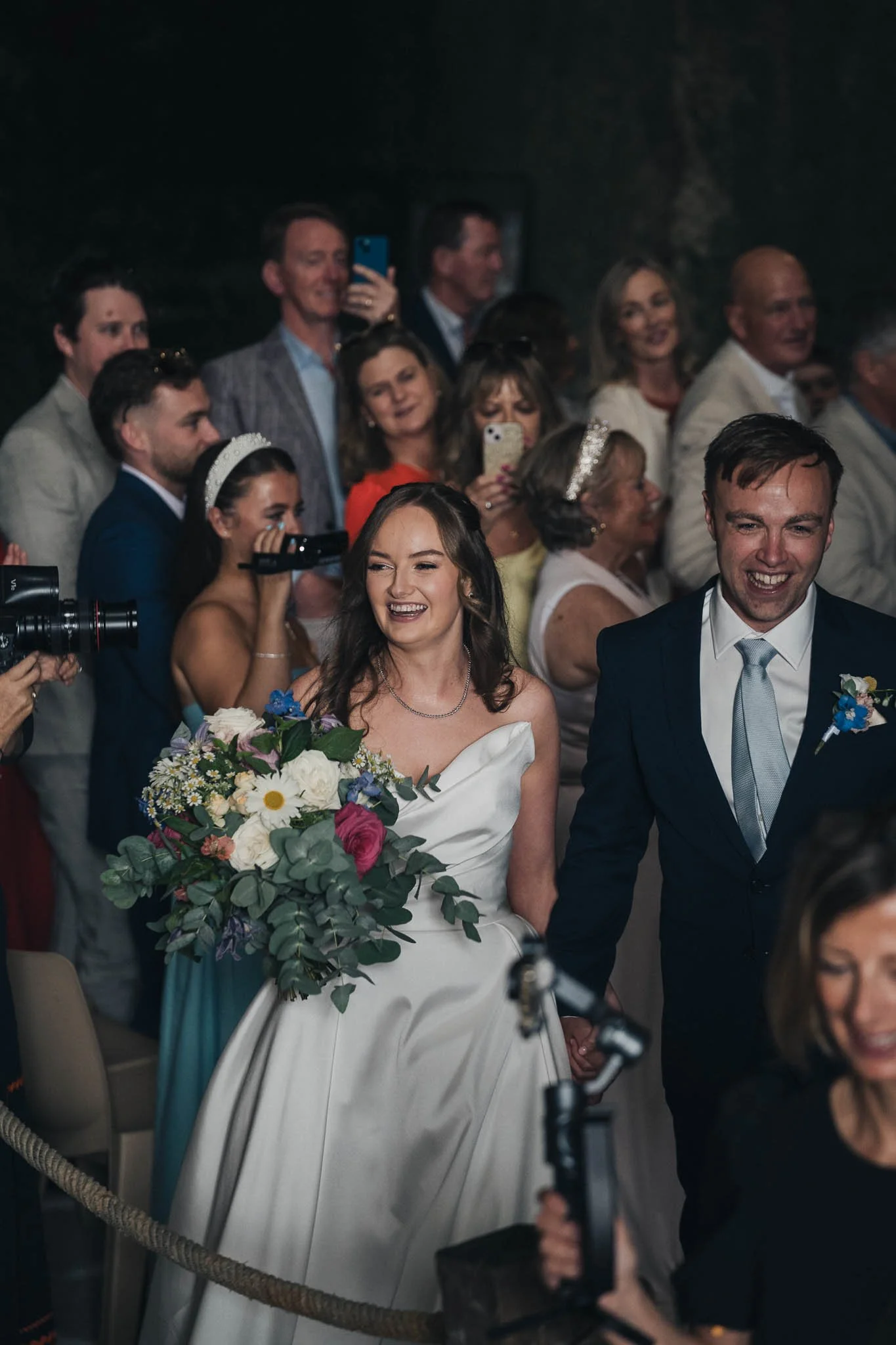 Bride and groom walking through the crowd after the ceremony, holding bouquets and smiling.