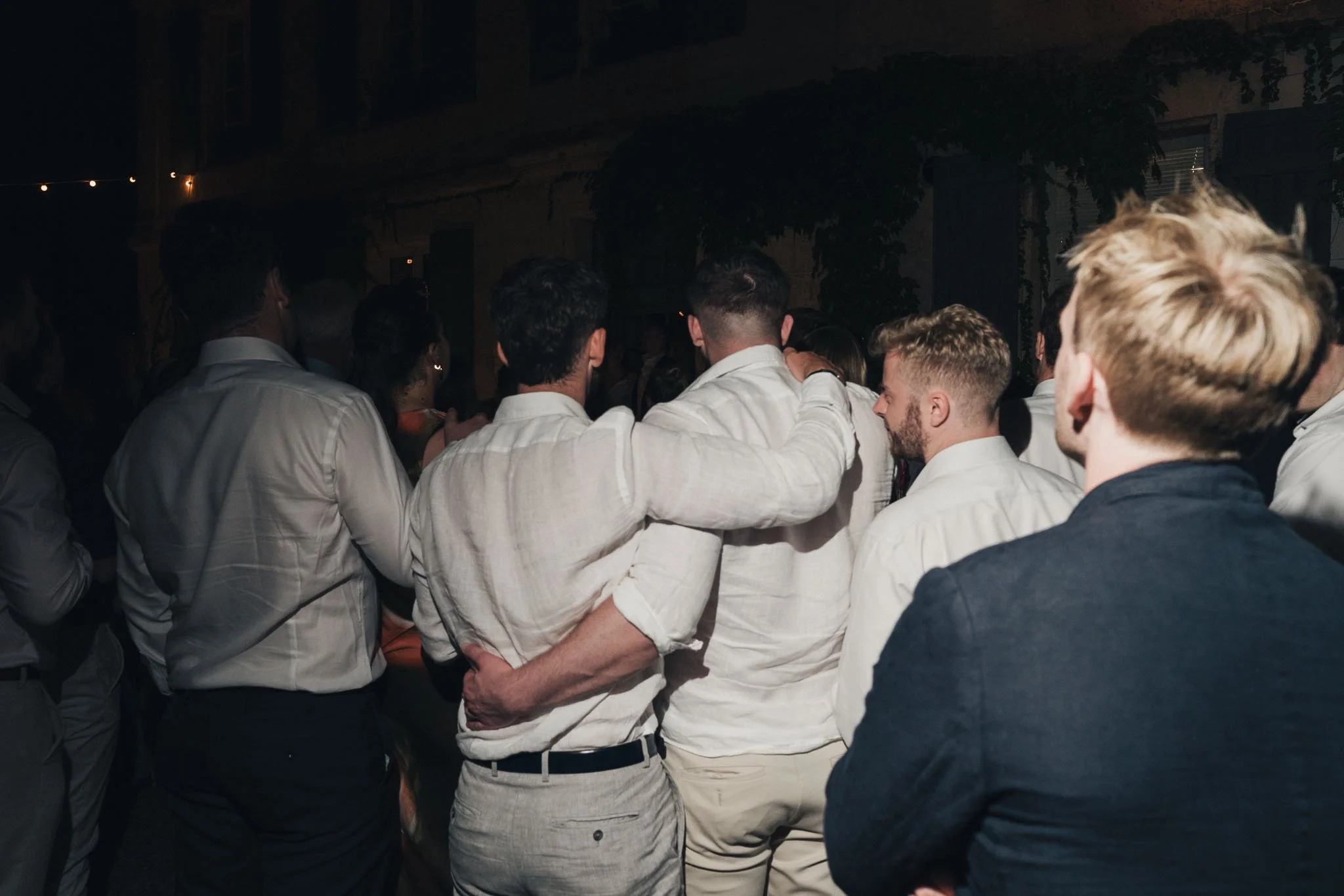 Group of guests standing arm-in-arm during a late evening moment at the wedding.