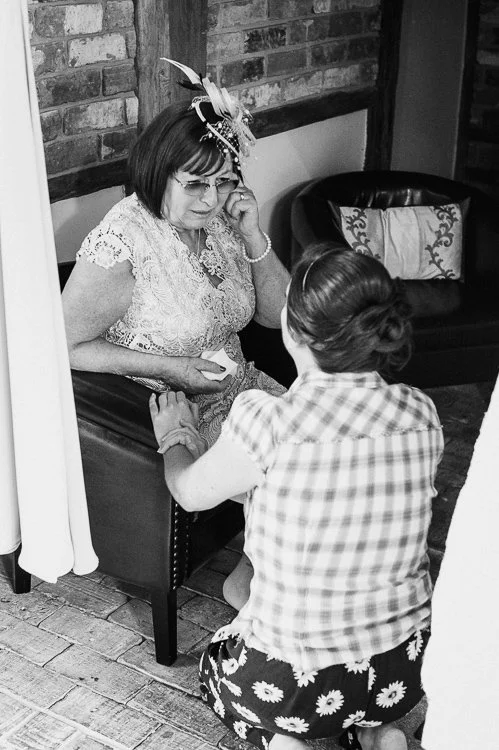 Emotional black and white photograph of a seated older woman holding hands with the Bride during a wedding, a quiet moment of connection.