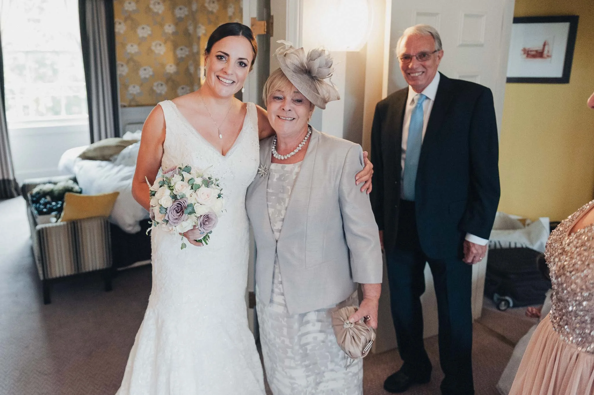 Bride standing with a family member during the morning preparations, holding her bouquet and smiling.