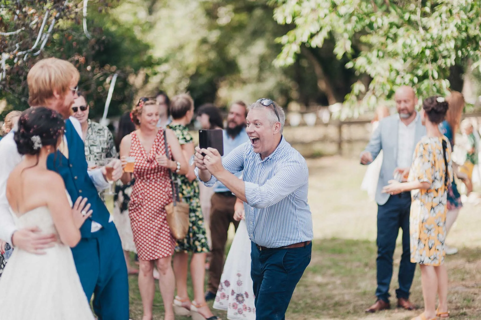 Guests laughing and taking photos during the drinks reception on the lawn.