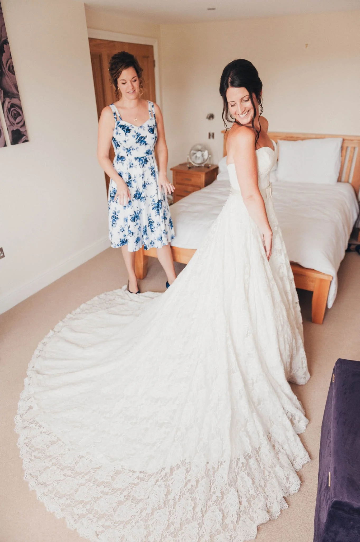 The bride standing in her wedding dress while a bridesmaid adjusts the long train.