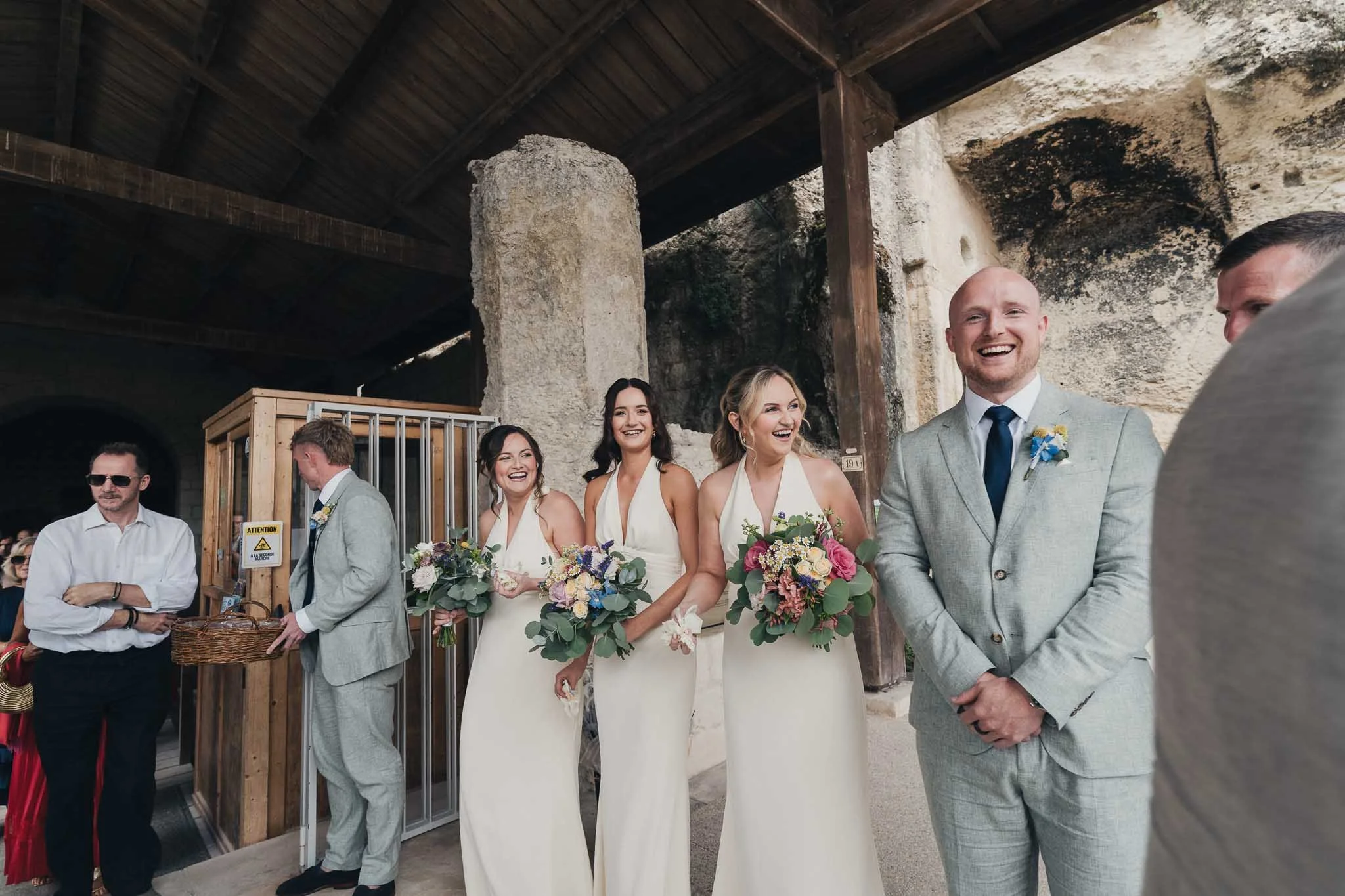 Bridesmaids and groomsman waiting with bouquets and confetti cones outside the Église Souterraine Saint-Jean.