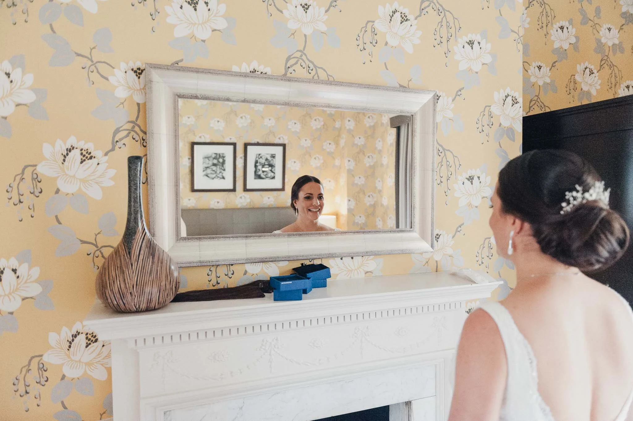 Bride looking at herself in the mirror before leaving for the ceremony, captured in soft window light.