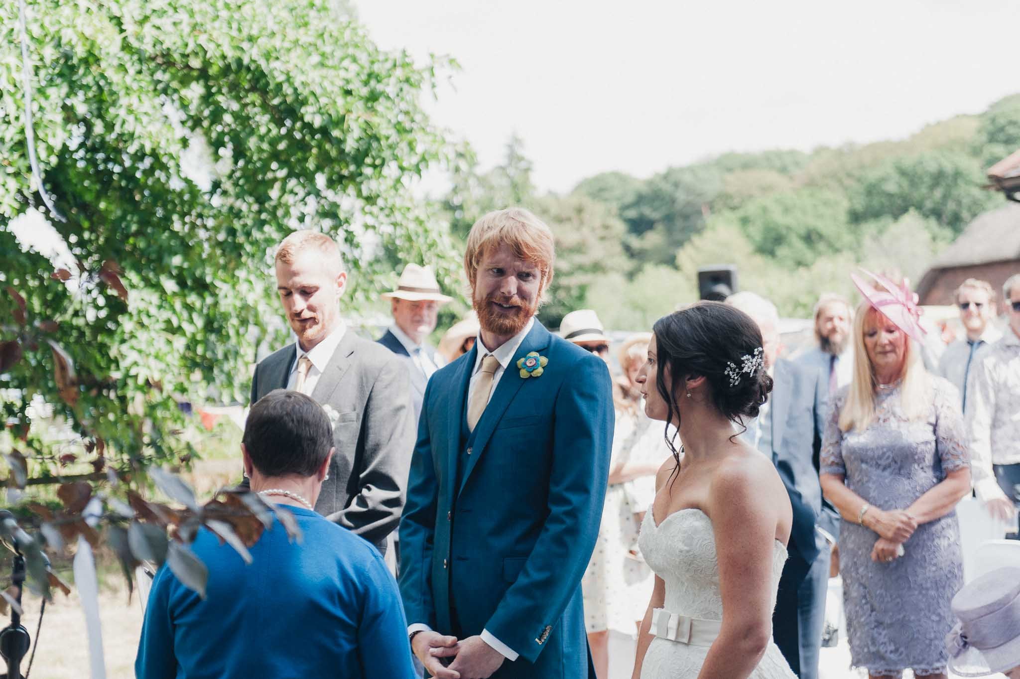 The groom smiling as the bride reaches the front of the aisle during the outdoor ceremony.