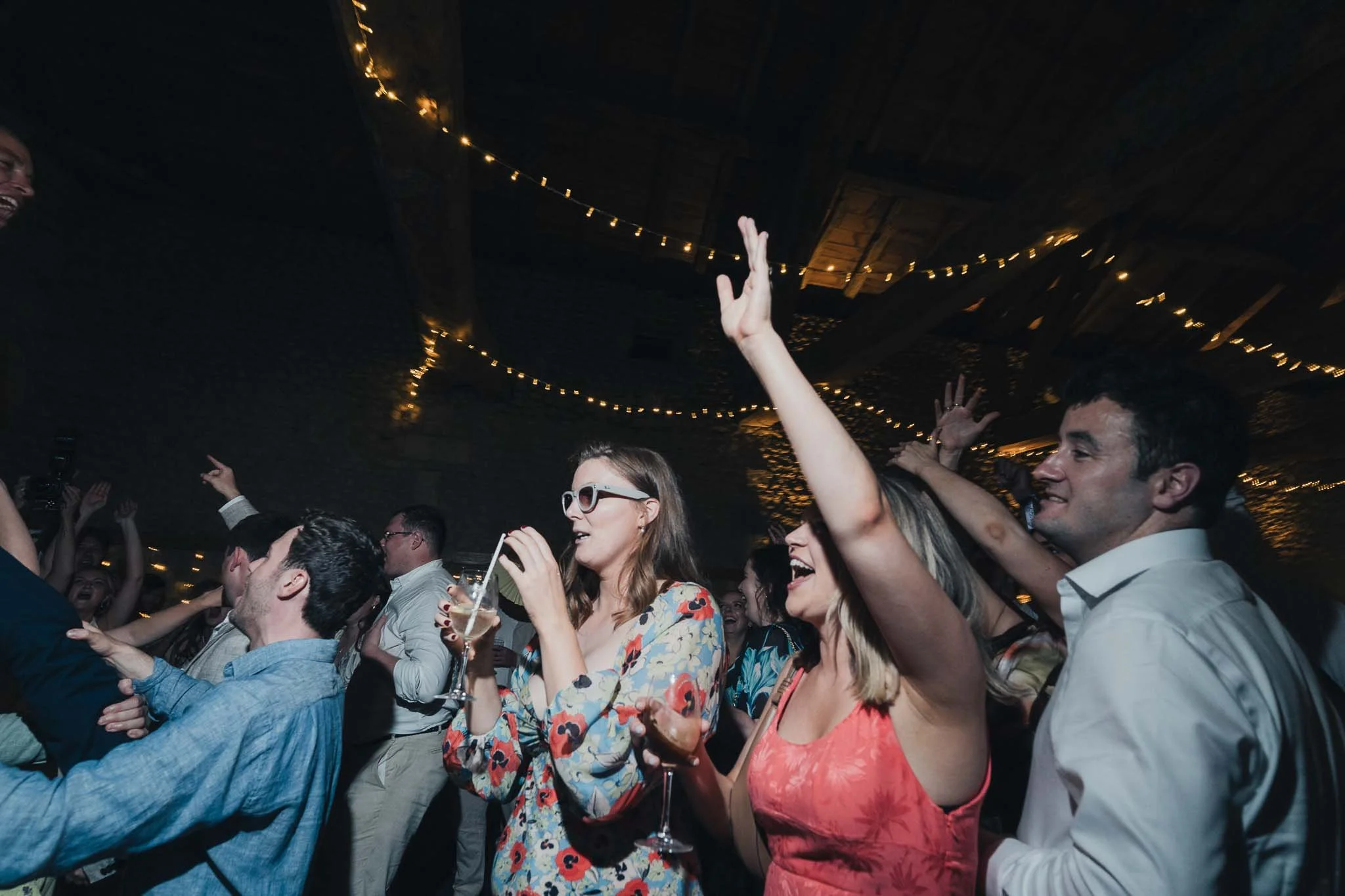 Guests dancing and cheering under string lights during the wedding party.