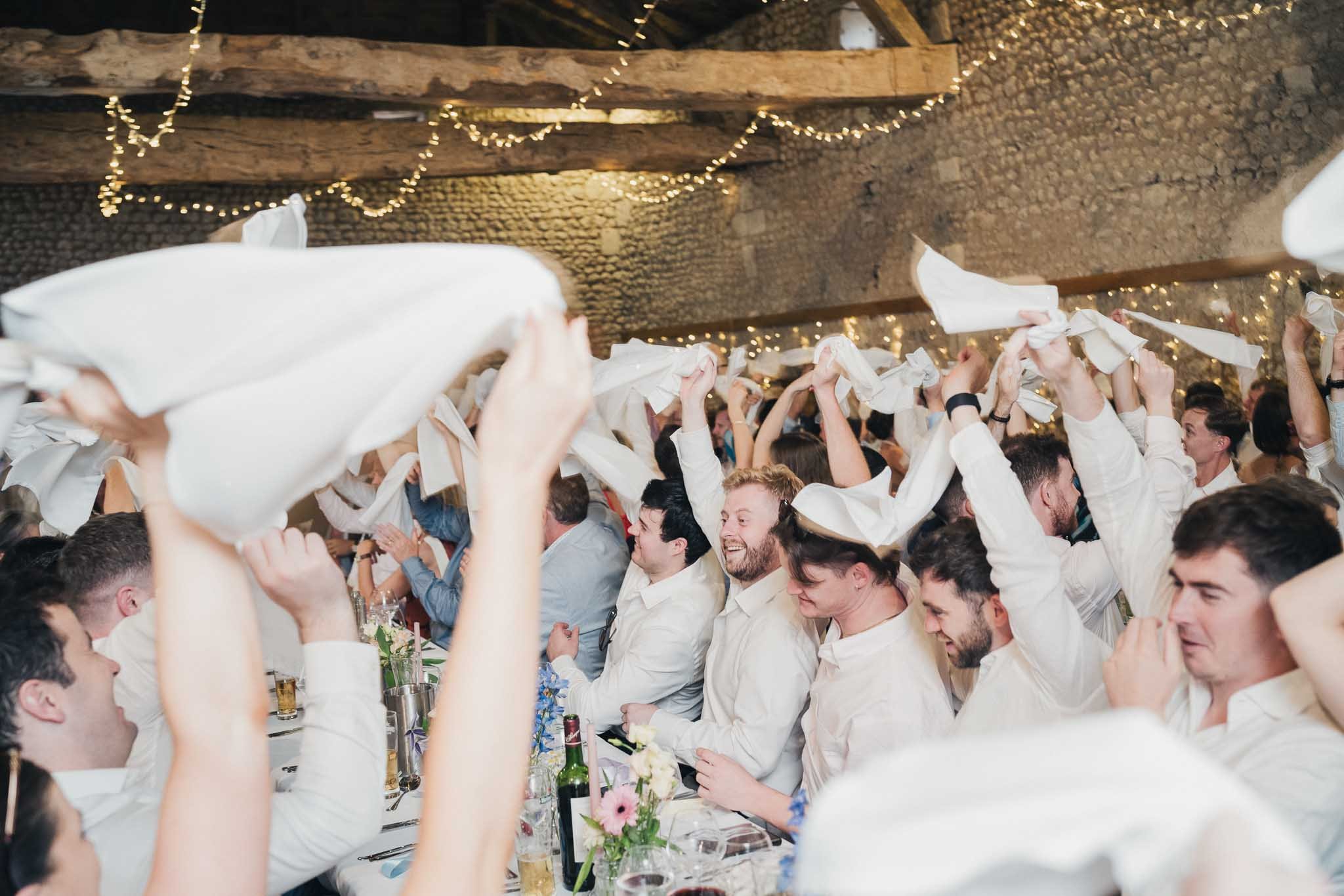 Guests waving napkins above their heads during a lively moment at the wedding dinner.
