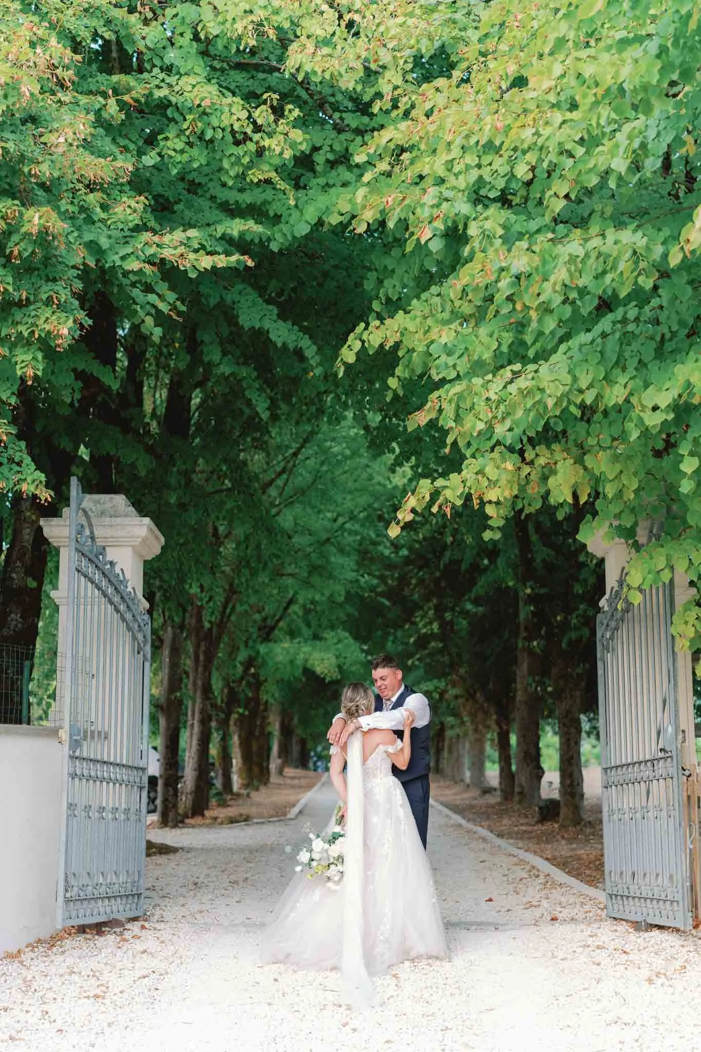 Bride and groom embracing and walking away through a tree tunnel at Paradis des Vignes, Charente