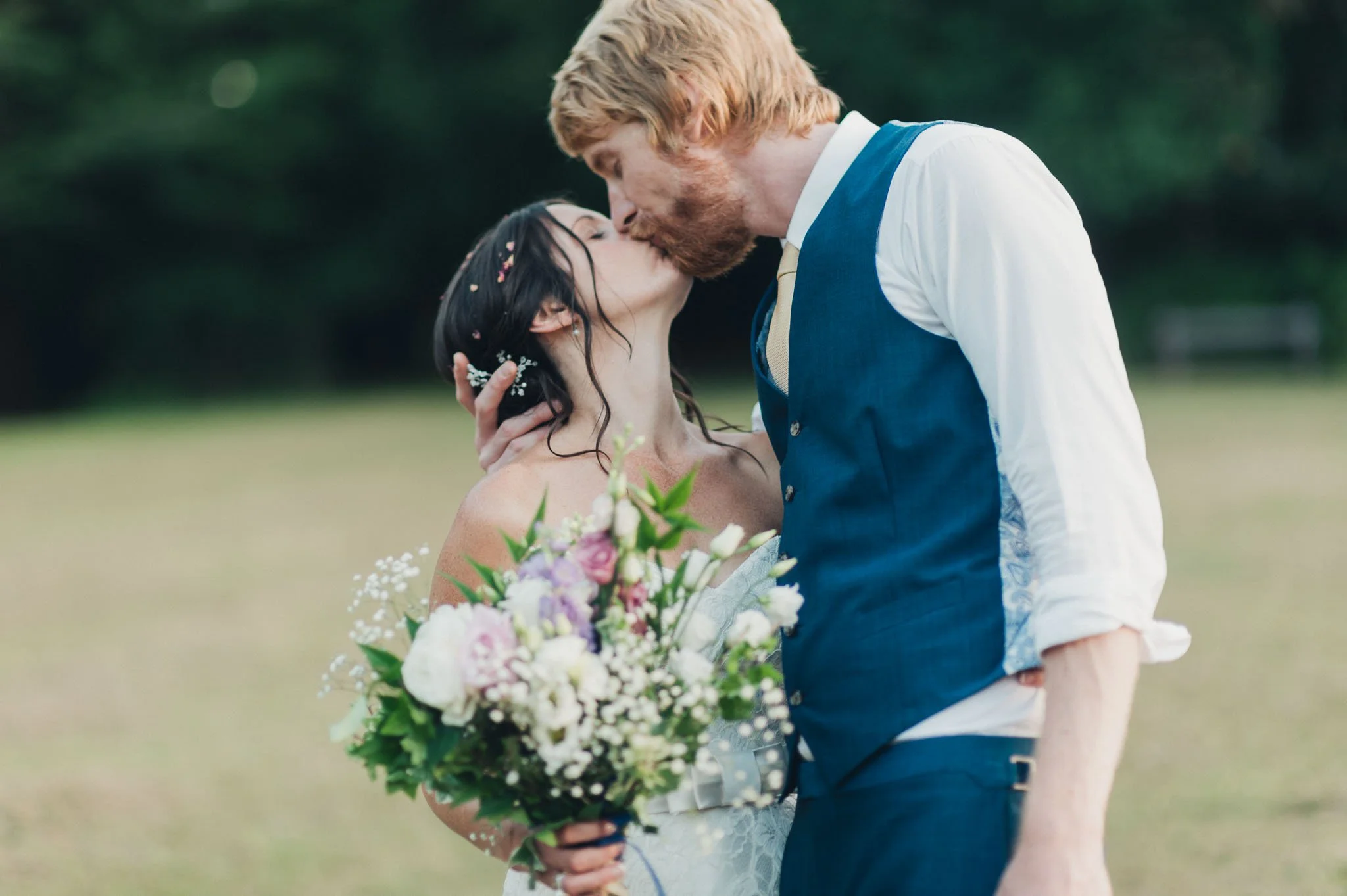 Close-up of the bride and groom kissing during their outdoor portraits, bouquet in the foreground.