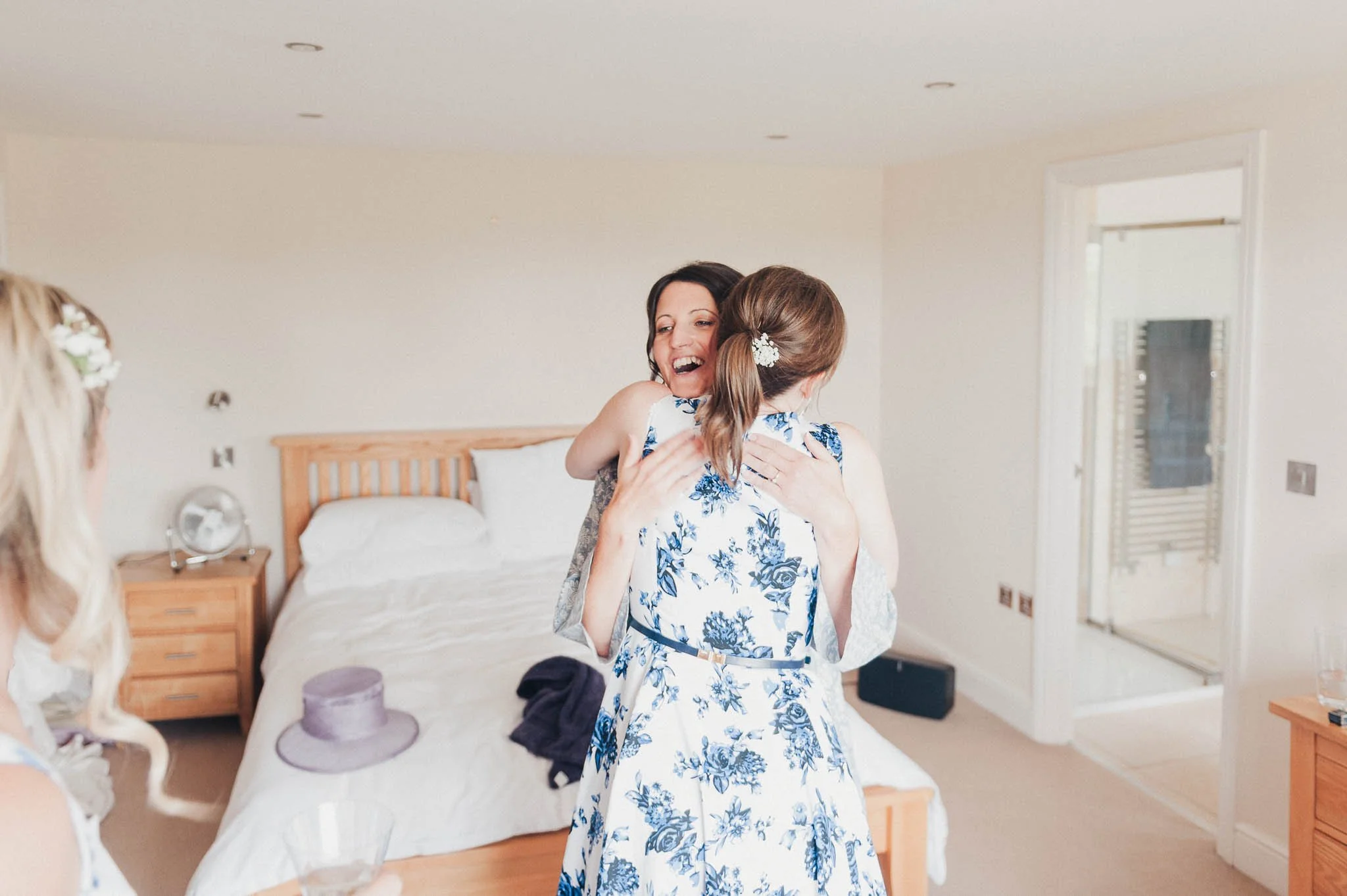 The bride hugging a bridesmaid in the bedroom during morning preparations.