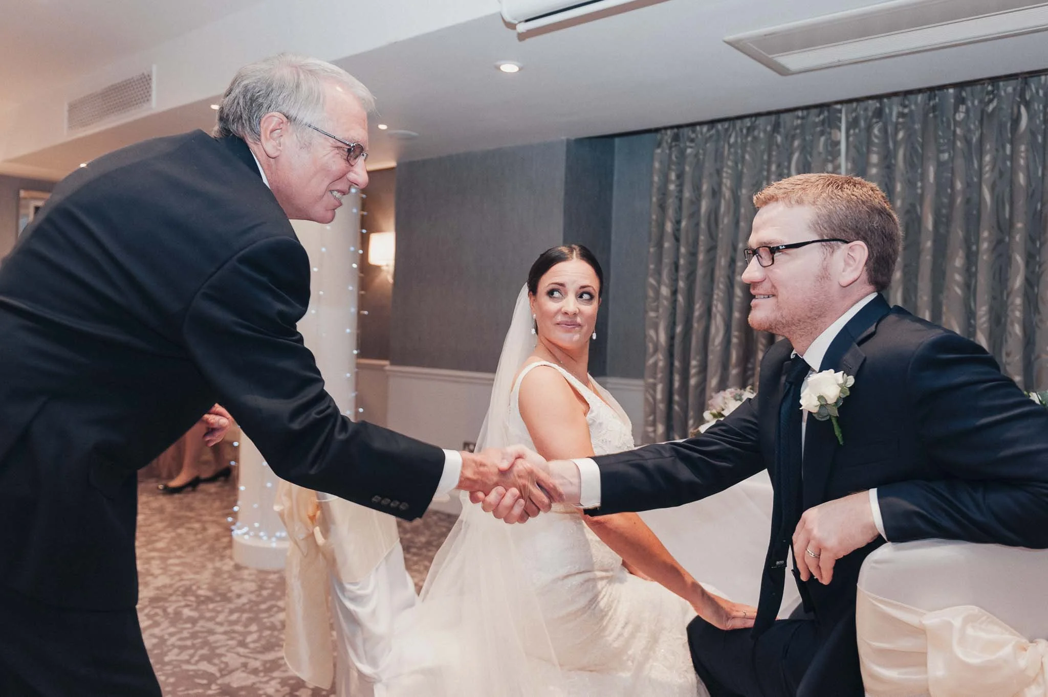 Family member shaking the groom’s hand at the start of the ceremony, with the bride watching.