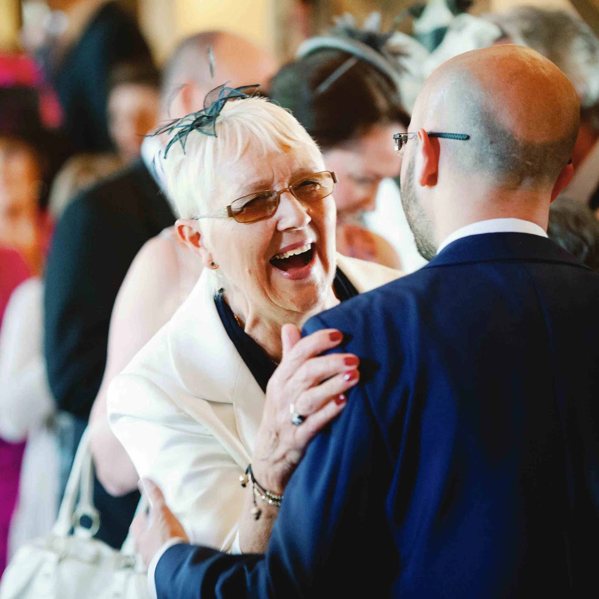 An older wedding guest laughing with the groom during a relaxed moment, showing natural connection and atmosphere at a wedding in South West France.