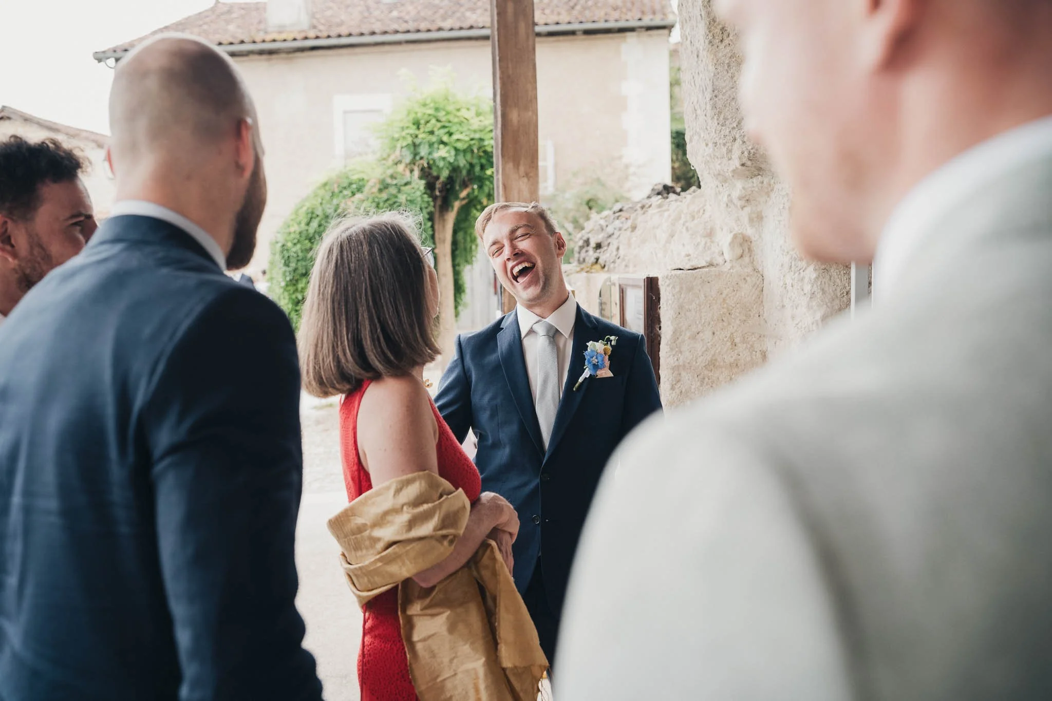 Groom laughing with guests during arrivals at Saint-Jean de Aubeterre-sur-Dronne.