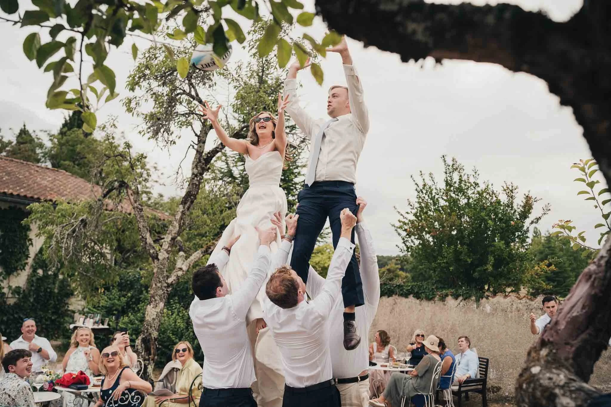 Bride and groom being lifted into the air by guests during a celebratory moment.