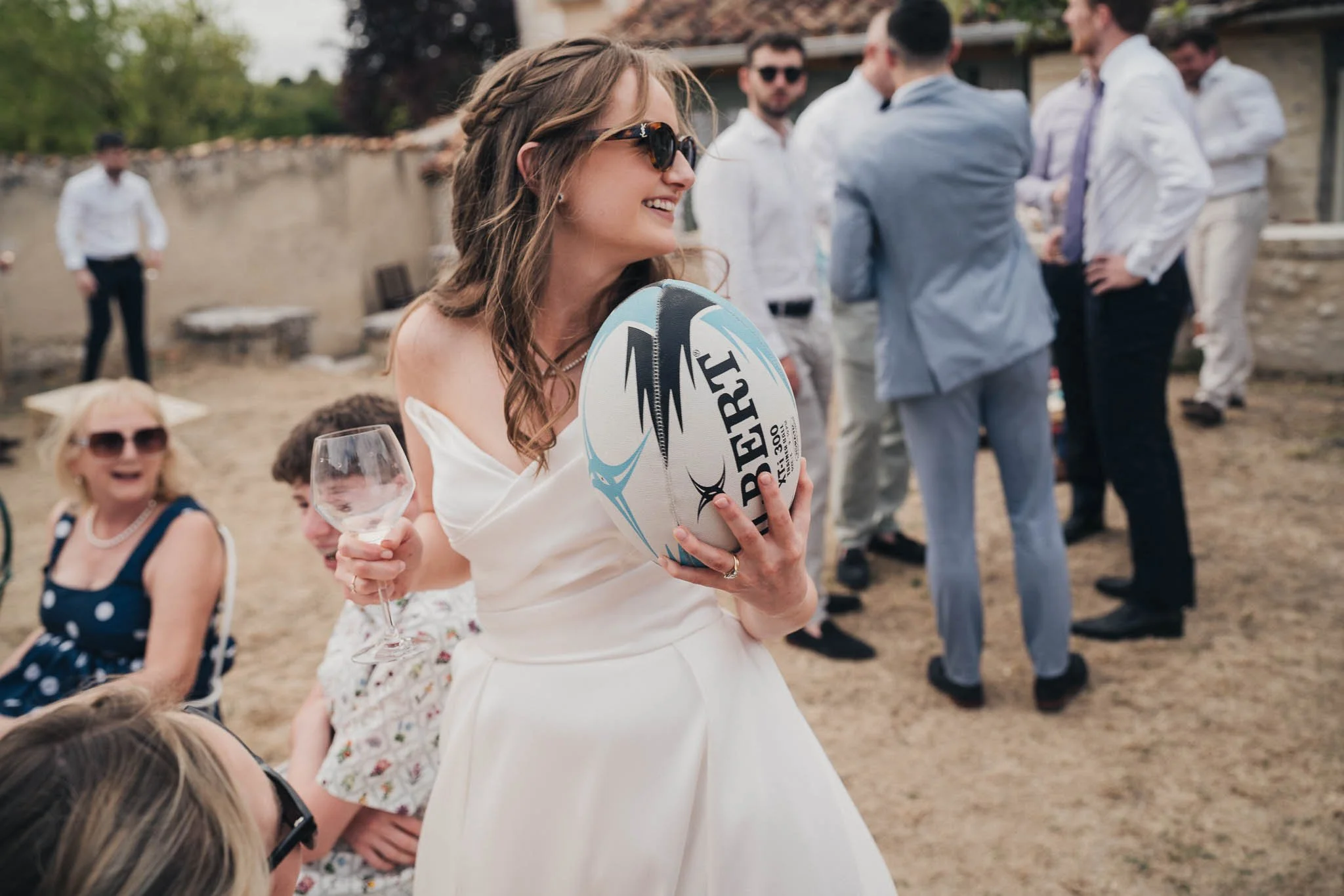 Bride smiling and holding the rugby ball while chatting with guests at the reception.
