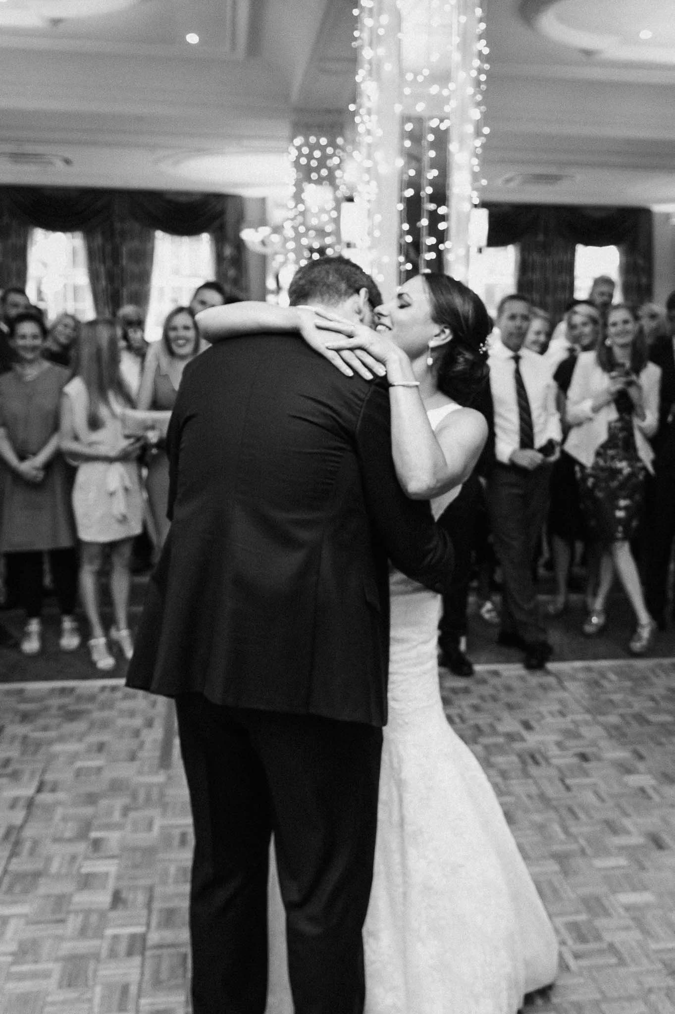 The couple sharing a warm hug on the dance floor as guests watch.