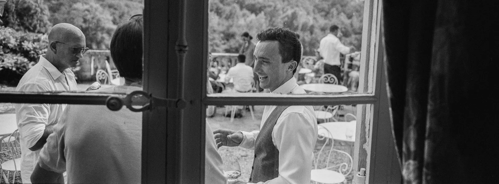 Black and white panoramic XPan film photograph of guests seen through a window at Château Lagorce