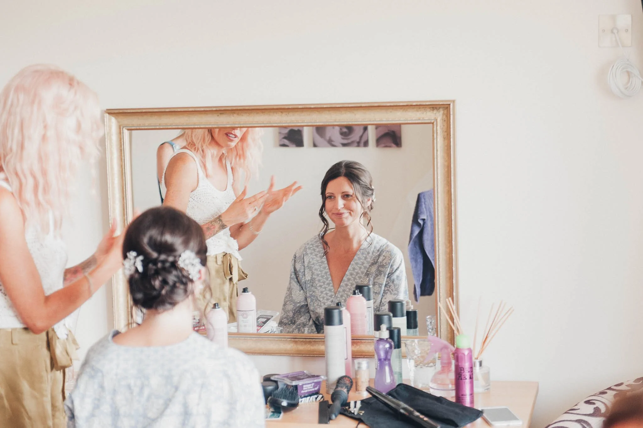 The makeup artist adding final touches to the bride’s makeup, reflected in the mirror.